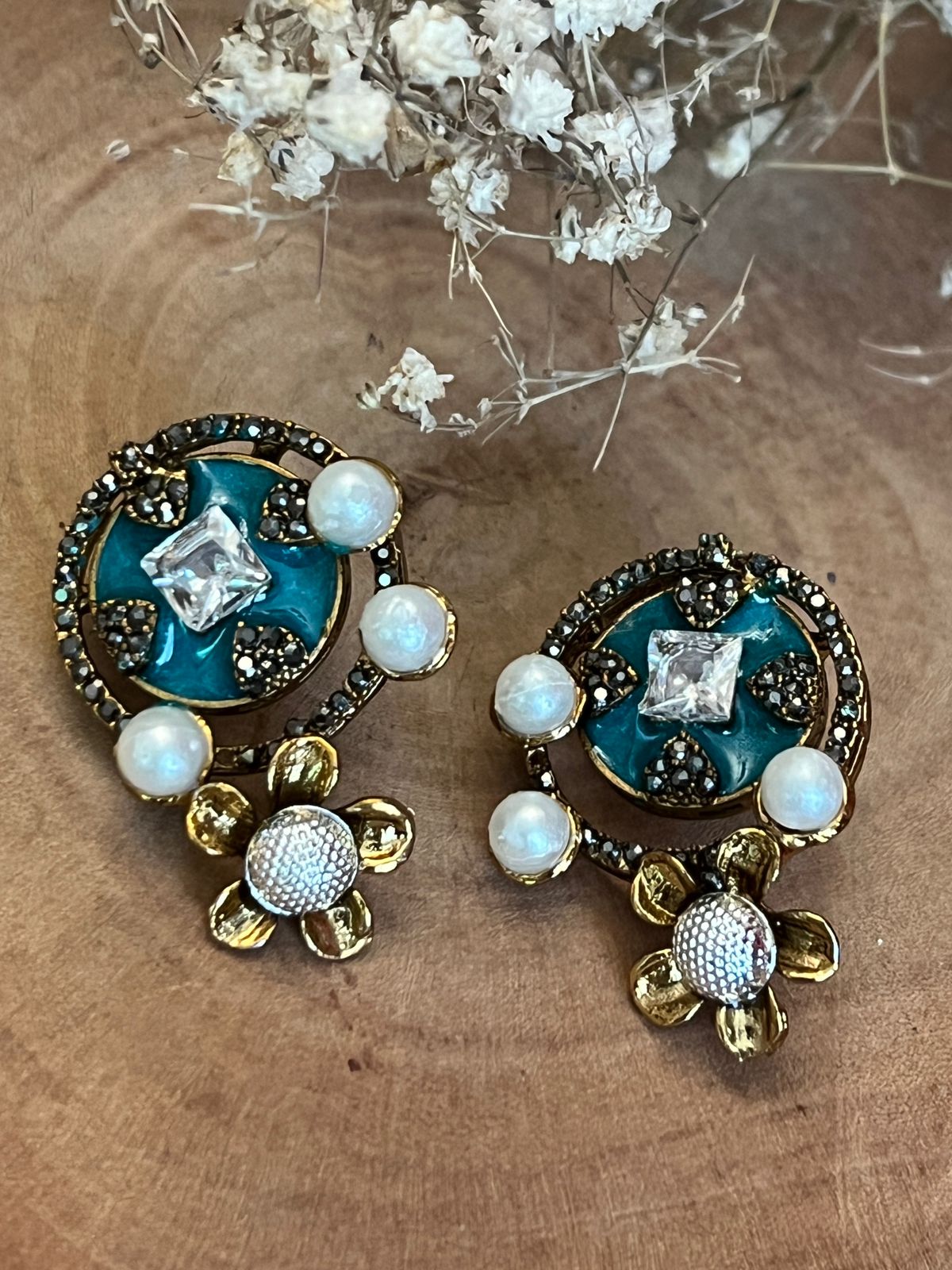 Teal and gold earrings with pearls and floral detailing on wood