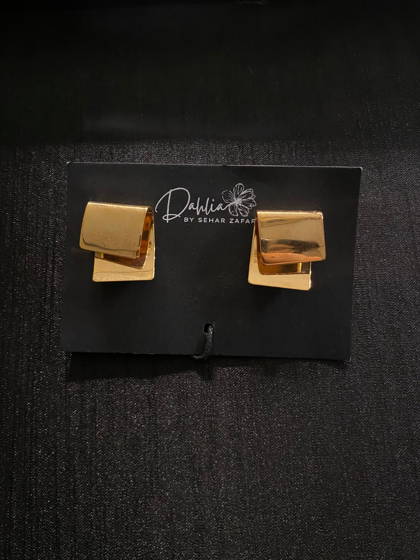 Matte gold geometric stud earrings displayed on a black Dahlia by Sehar Zafar card.
