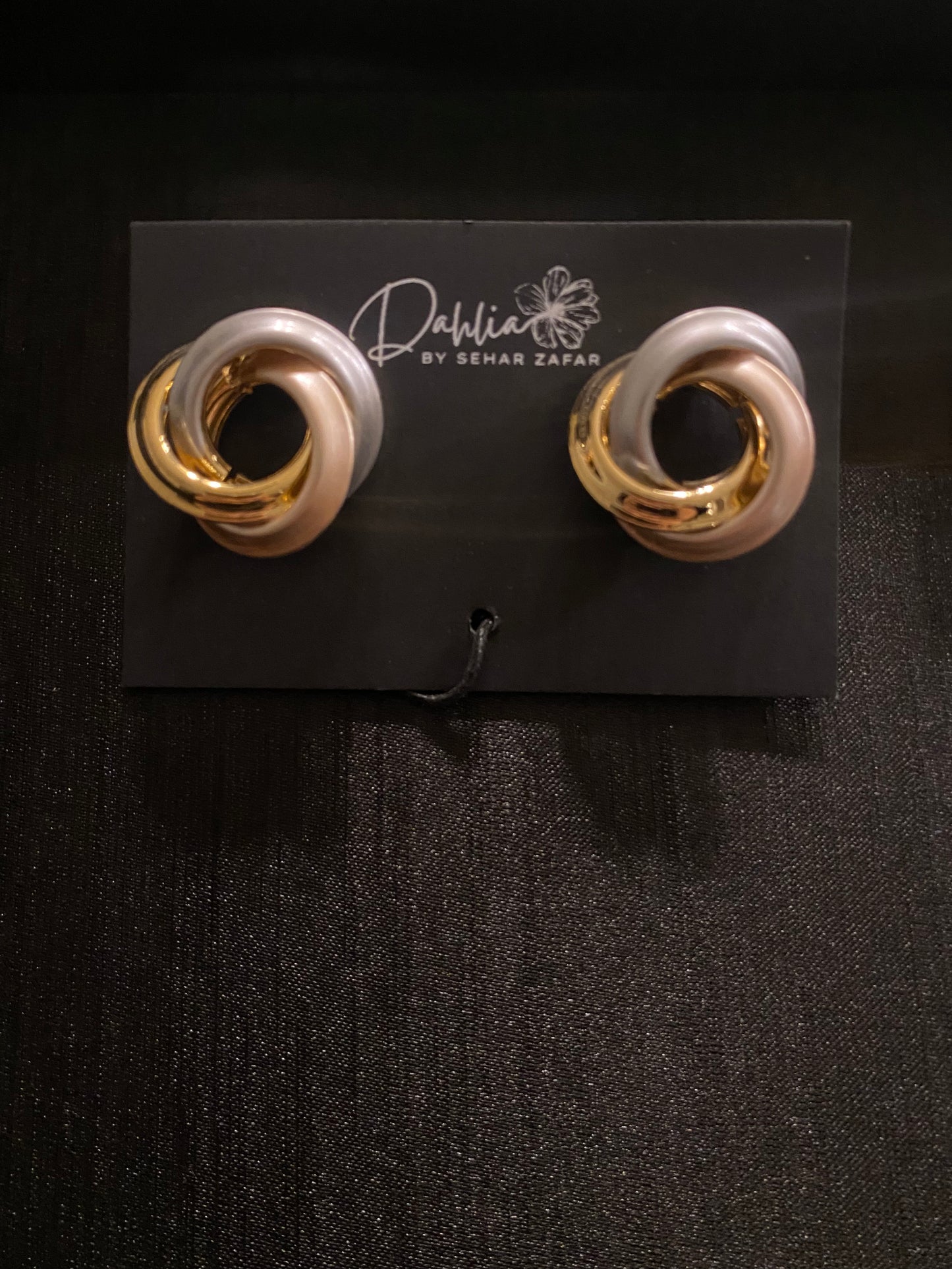 Twisted gold and pearlescent pink loop earrings on black branded card