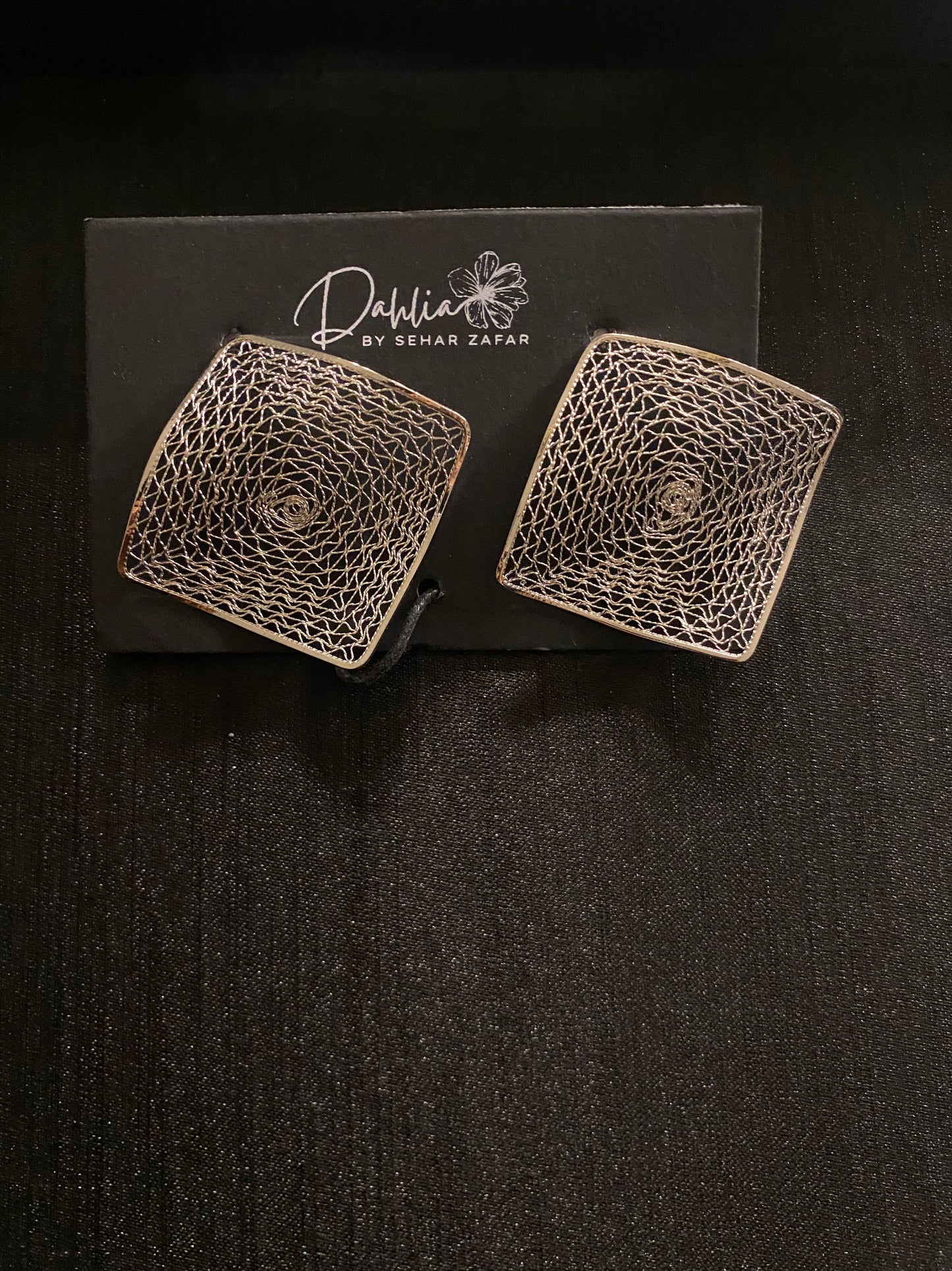 Square earrings with geometric web pattern on black branded card