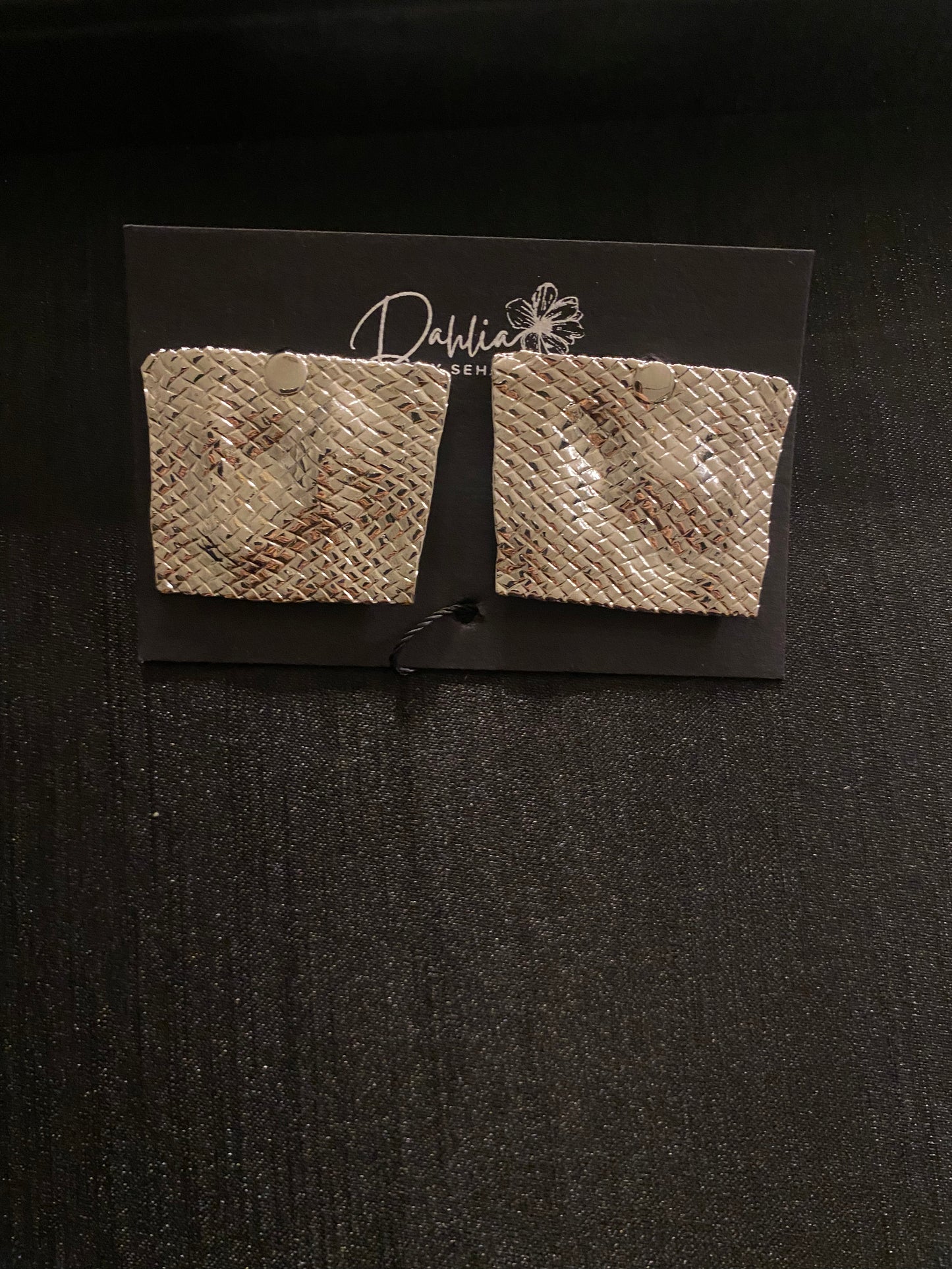 Gold square earrings with woven texture and curved shape on black branded card