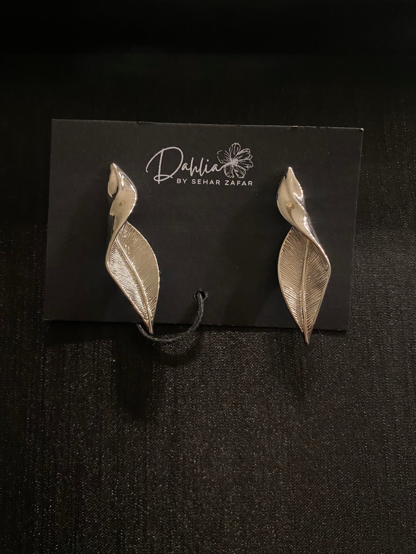 Silver leaf-shaped earrings with vein and petal detail on black branded card