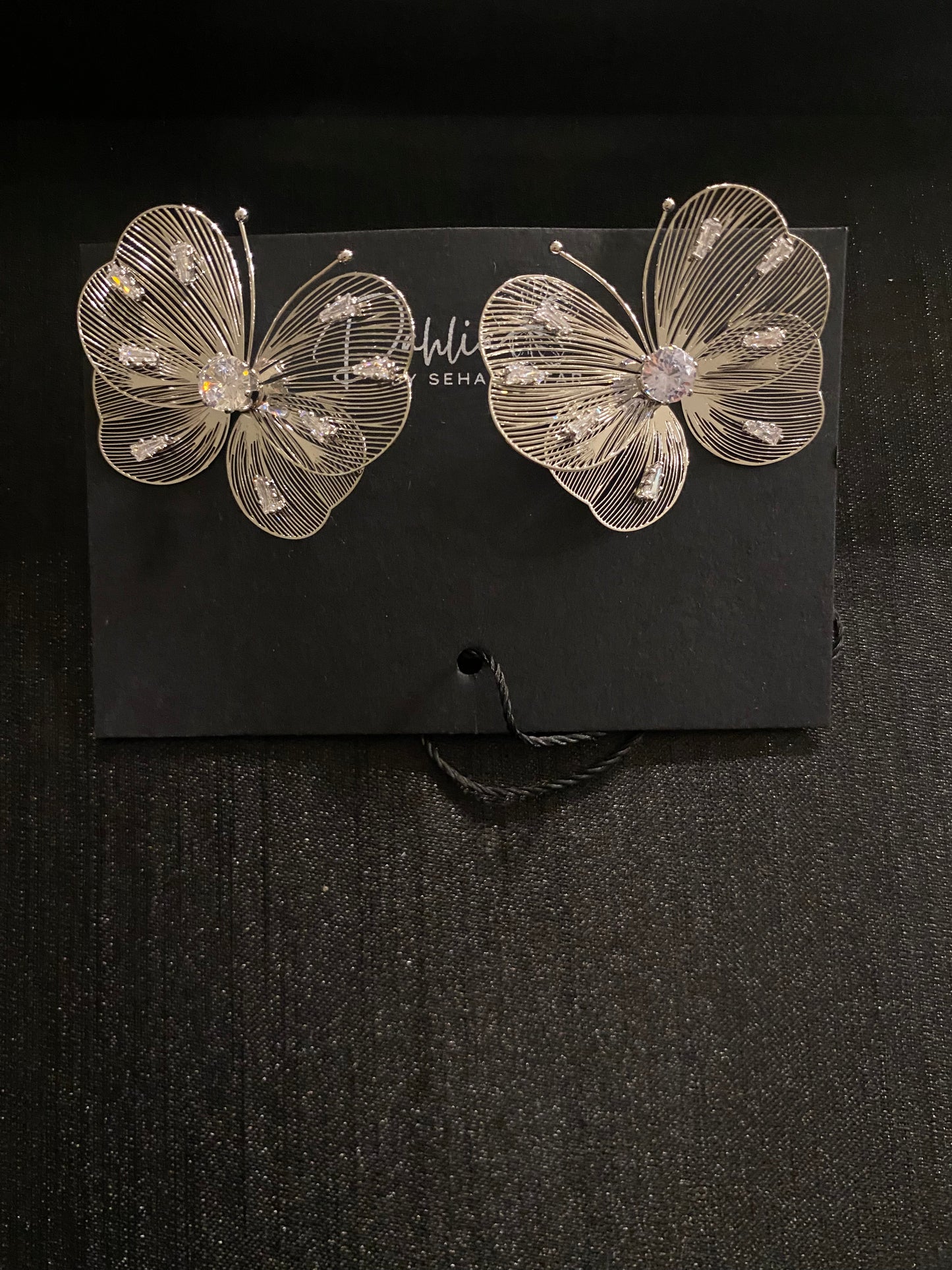 Gold wire butterfly earrings with gemstone wings on black branded card