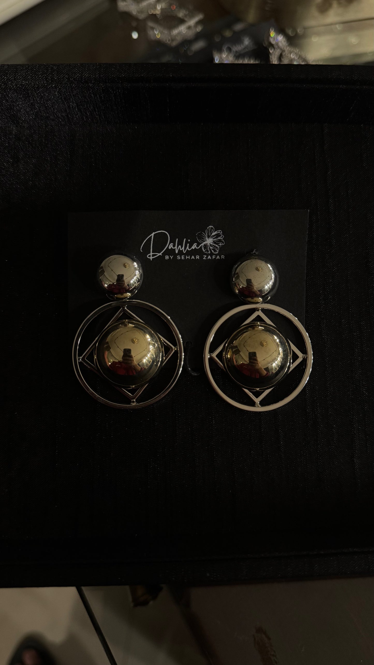 Gold and silver geometric earrings with circular and square frames on black branded card