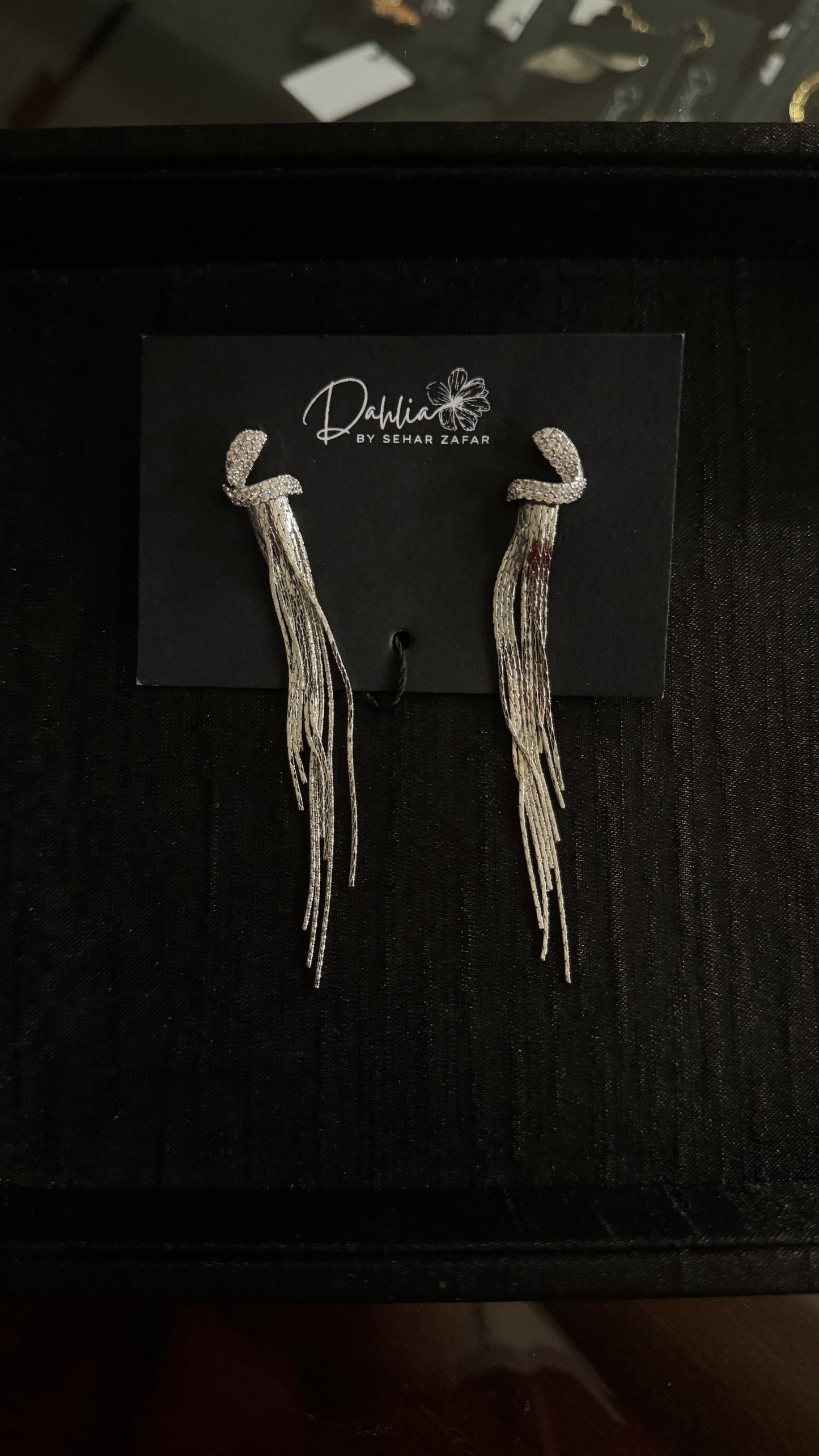 Silver knotted loop earrings with shimmering tassel strands on black branded card