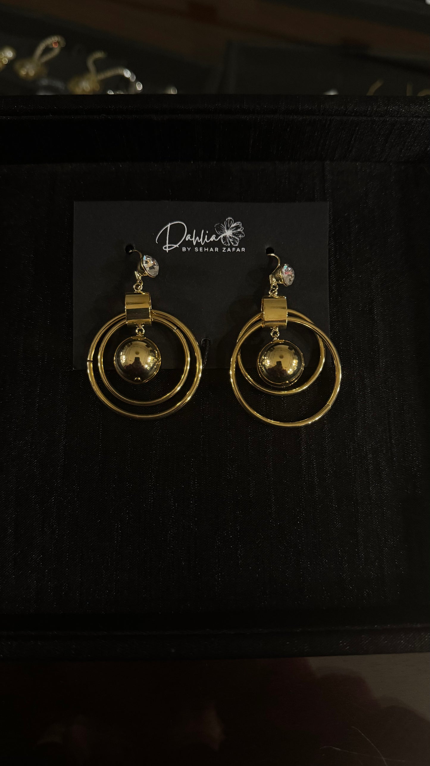 Gold double hoop earrings with central bead and gem stud on black branded card
