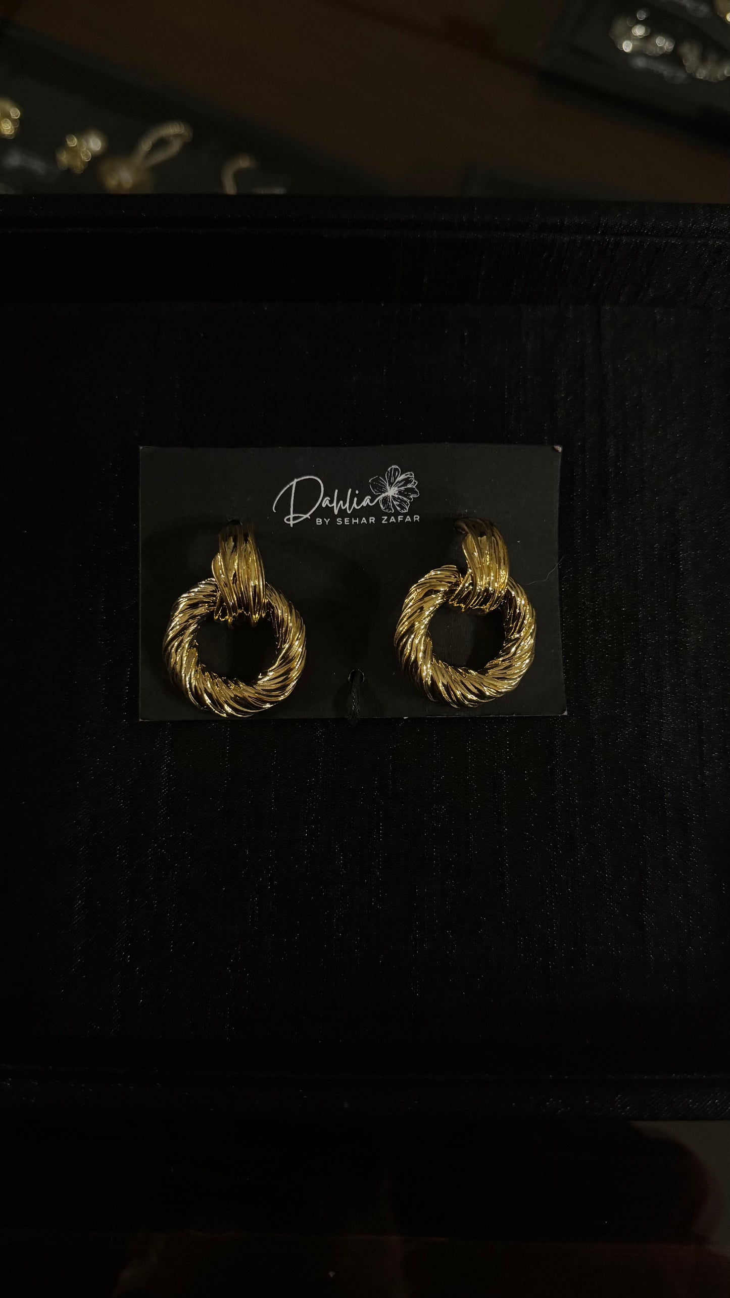 Gold textured hoop earrings with twisted rope design on black branded card