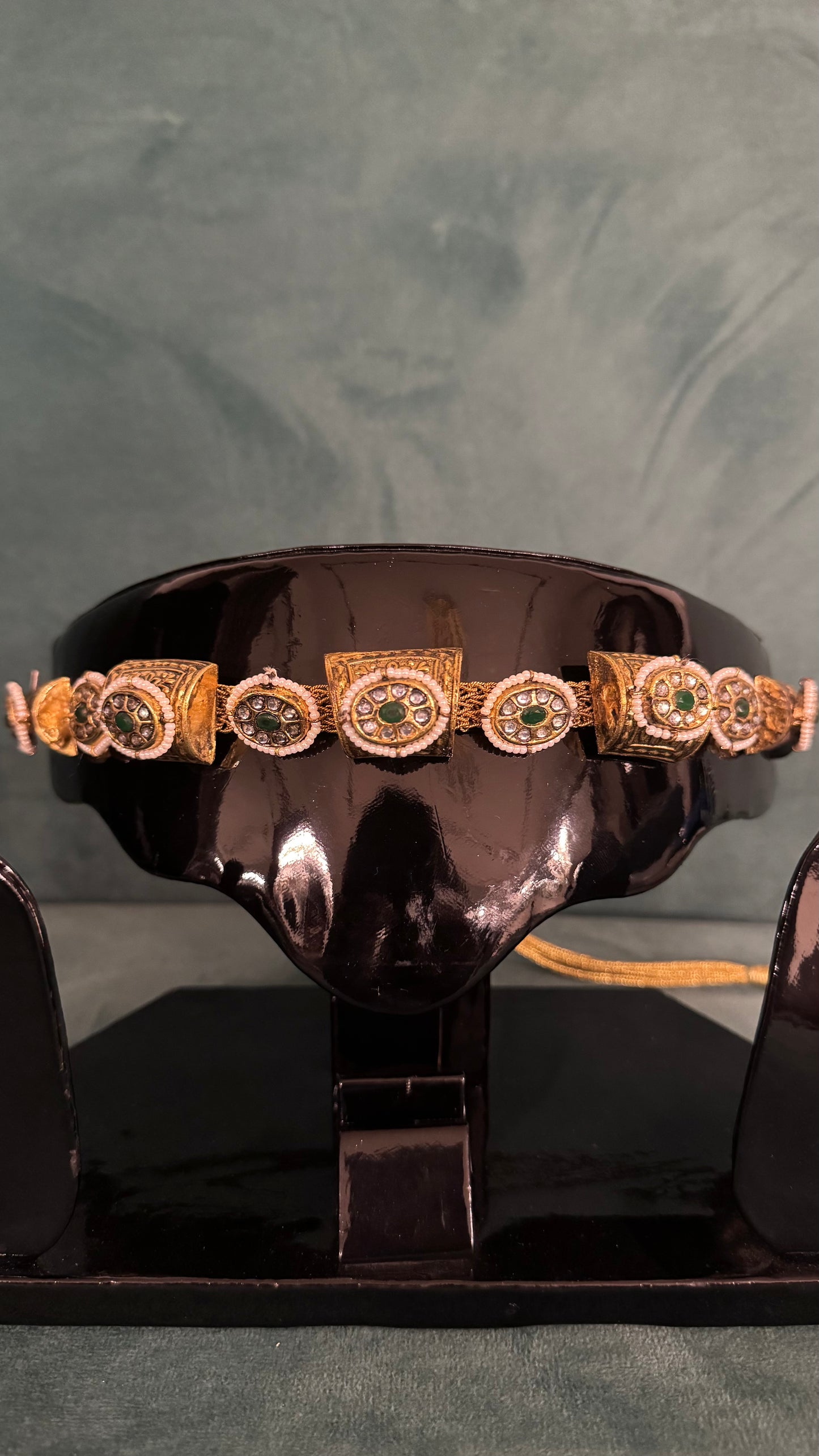 Gold choker necklace sets with green and white gemstone detailing on black display stand