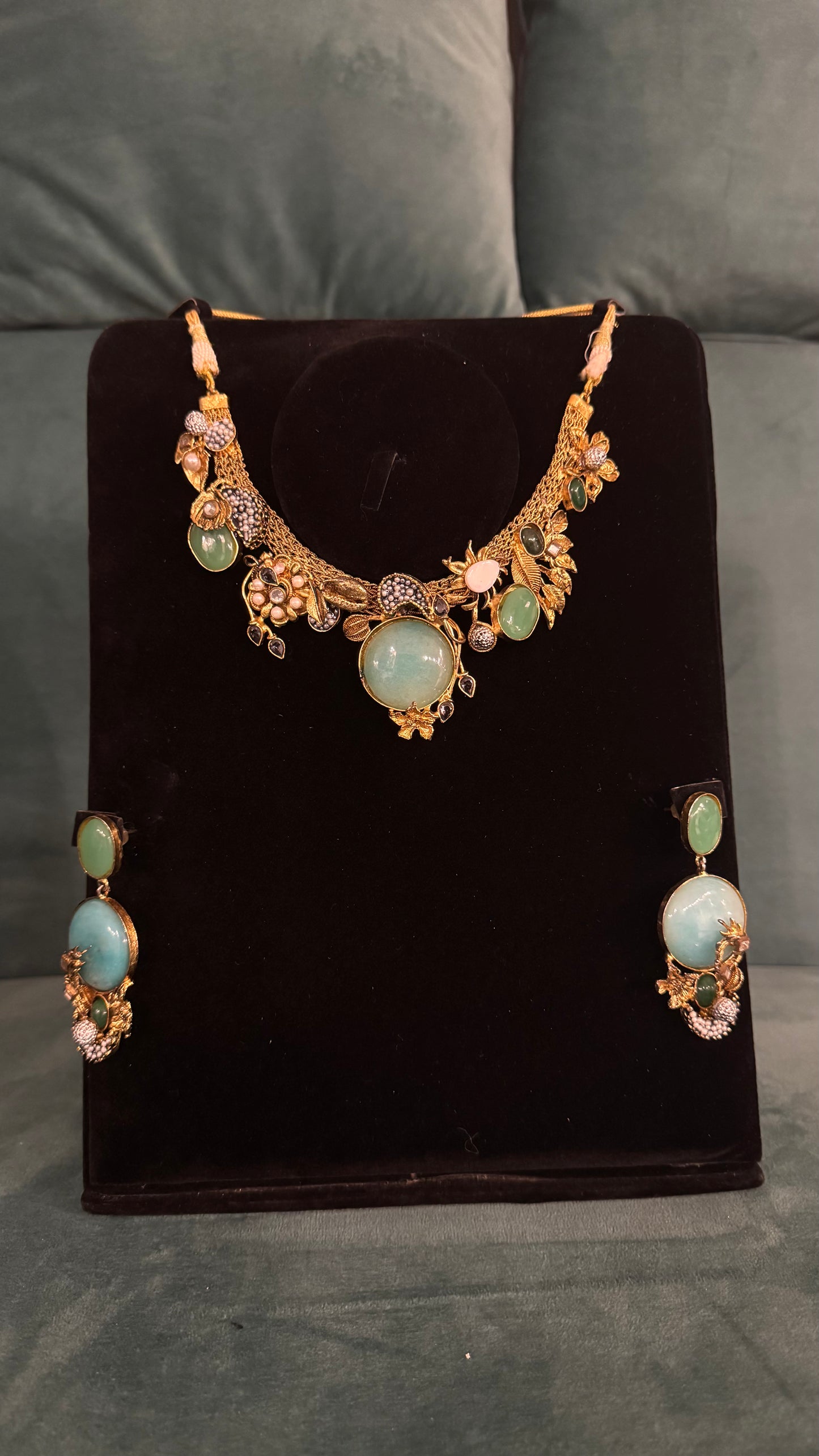 Traditional necklace sets with green gemstones, floral motifs, and gold detailing on black velvet stand