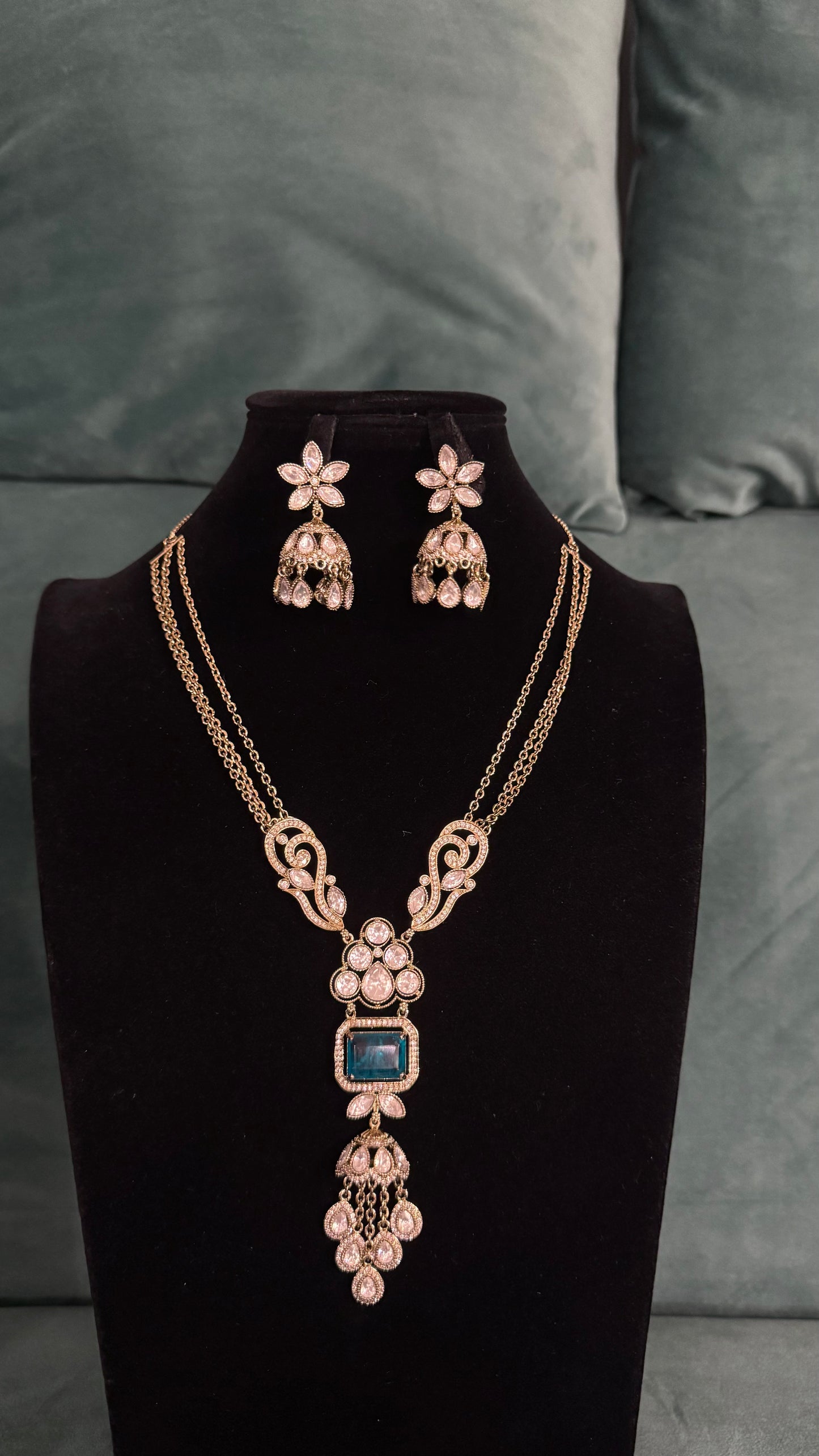 Elegant necklace sets with blue gemstone pendant, floral motifs, and gold chain on black velvet bust