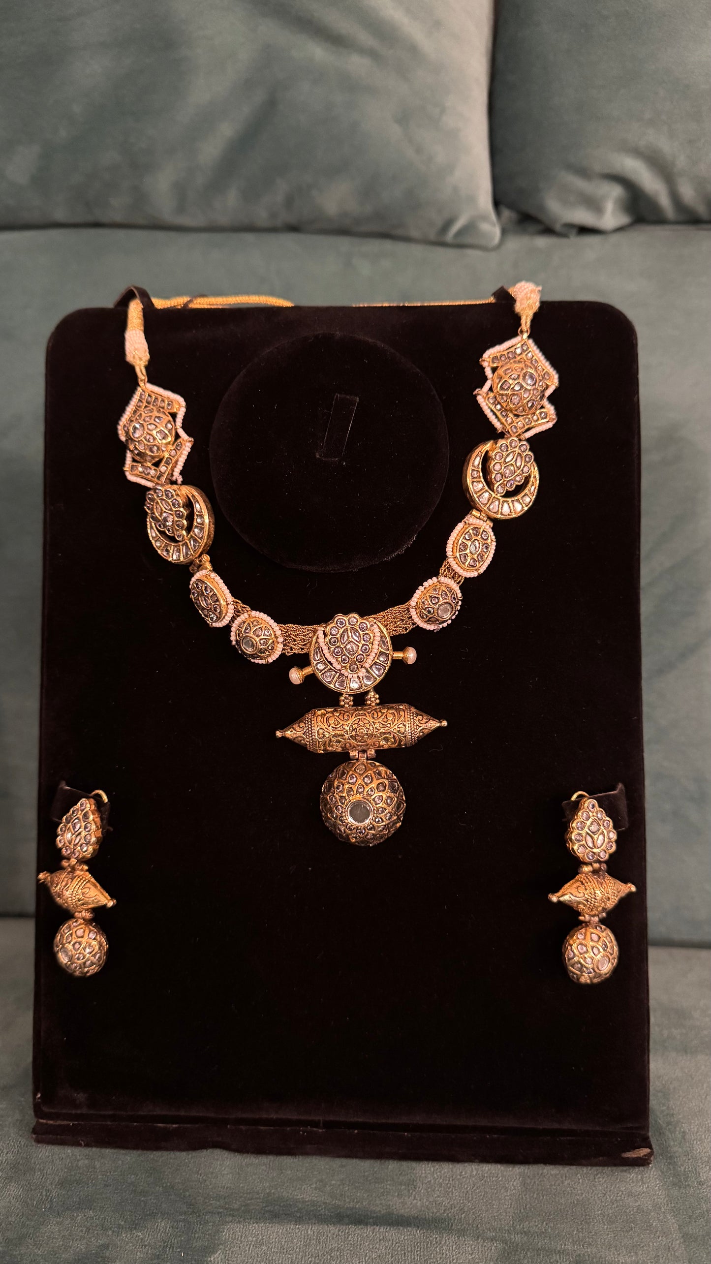 Traditional necklace sets with ornate gold filigree, spherical pendants, and geometric motifs on black velvet stand