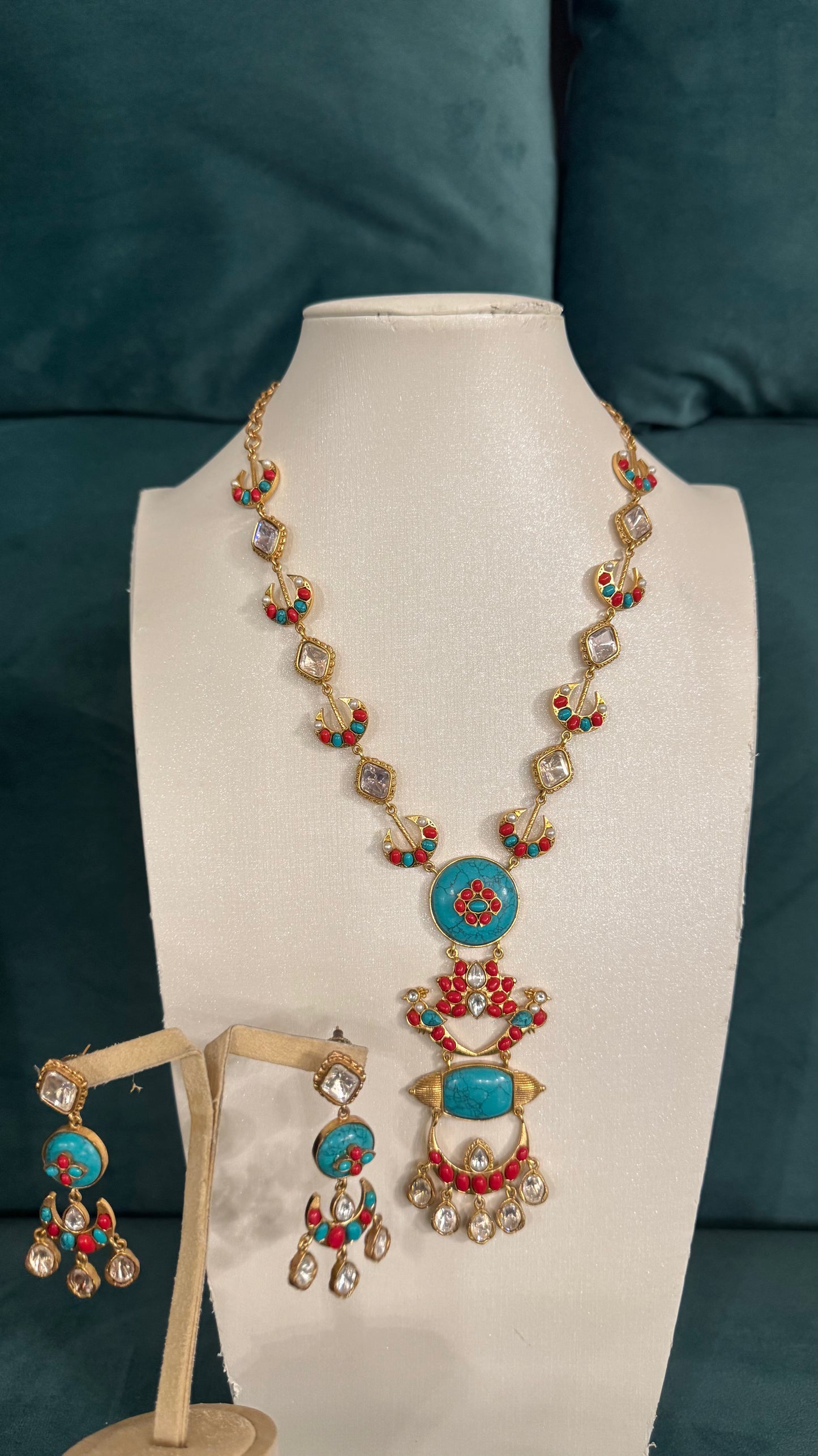 Traditional necklace sets with red floral motifs and turquoise teardrop pendants on white bust