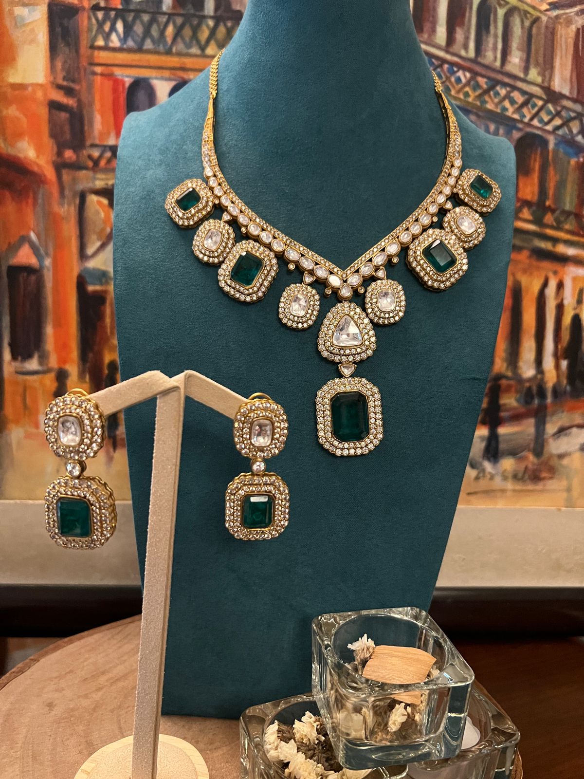Kundan necklace with square emerald stones and matching earrings displayed on a teal stand.