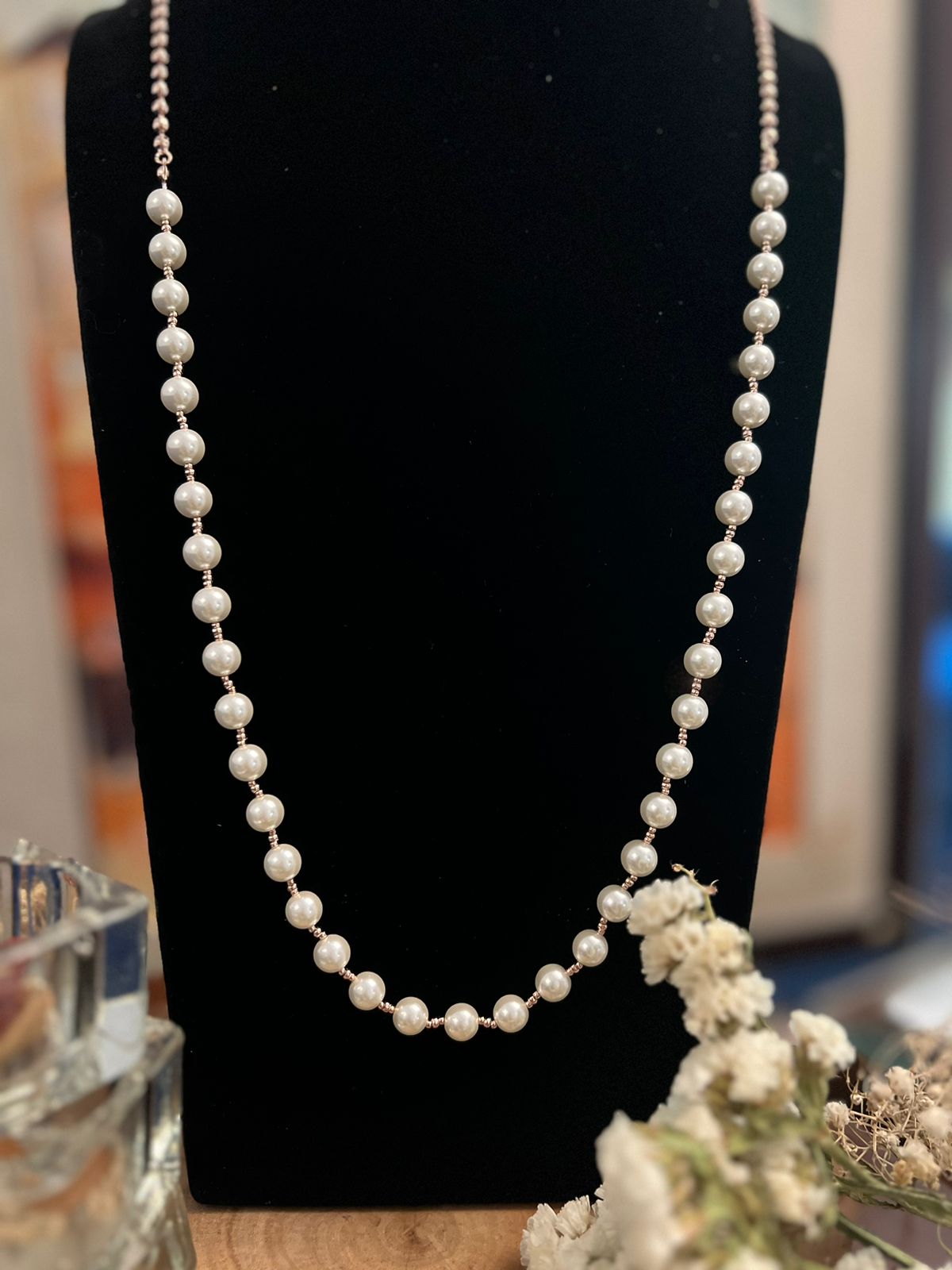 A white pearl long necklace displayed on a mannequin bust, with a classic design and a chain of pearls.