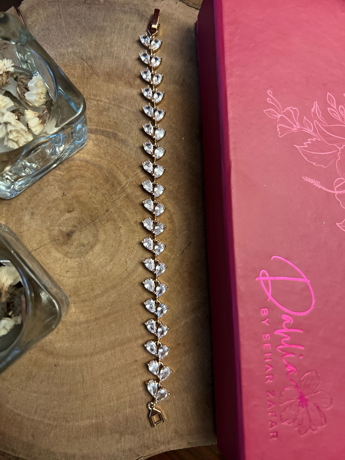 A bracelet with silver-colored beads and crystal embellishments, displayed on a wooden surface next to a pink-covered notebook with floral designs.