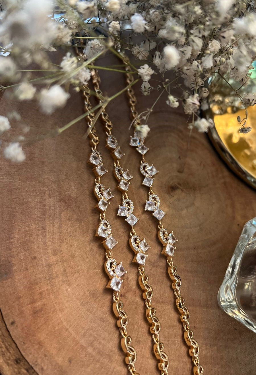A gold chain bracelet with small decorative elements on the chains, displayed on a wooden surface.