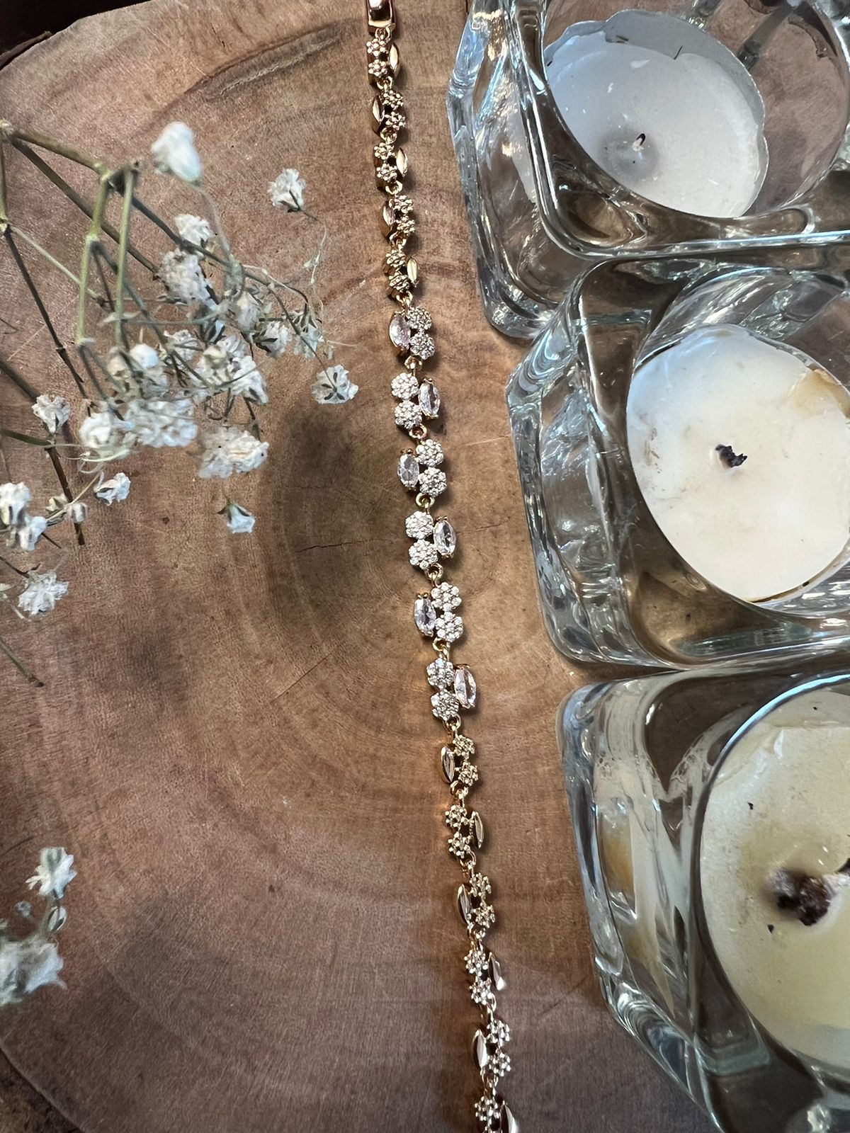 Gold floral bracelet with stone detailing displayed beside candles.