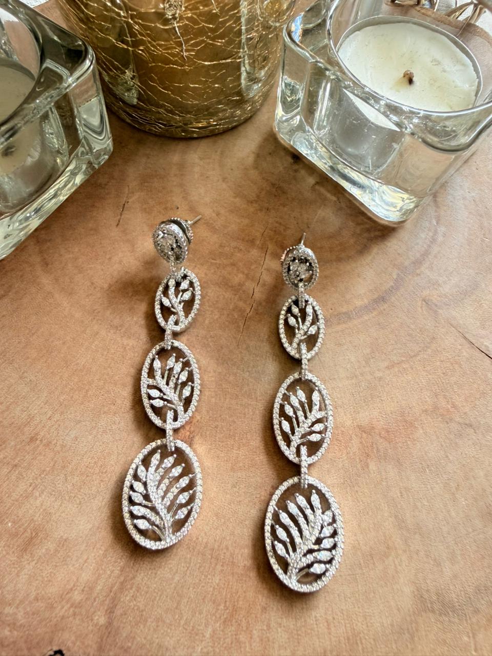 Silver leaf-shaped earrings on a wooden surface with candles in the background