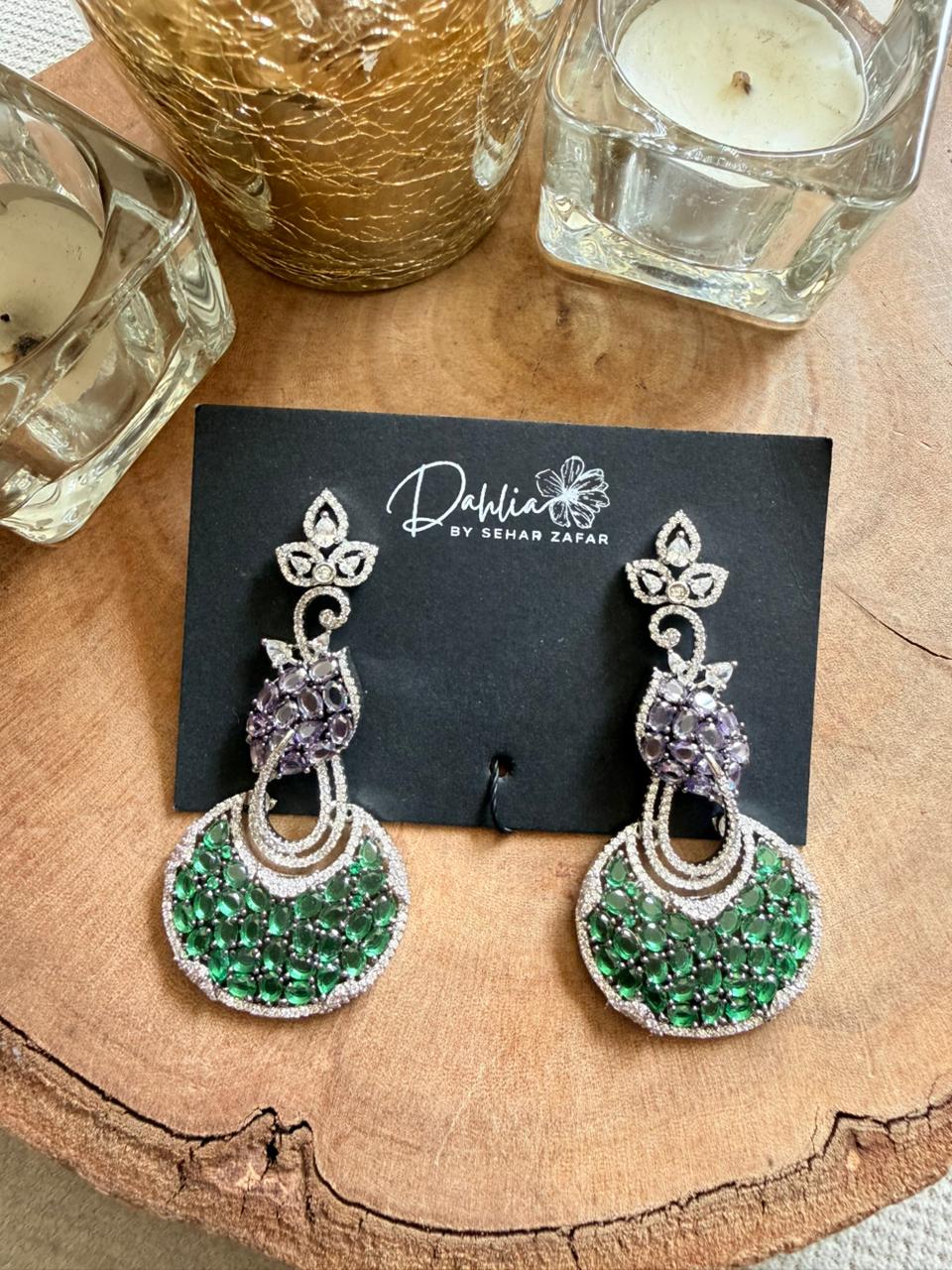 Green and silver earrings on a black card with 'Dahlia' branding, placed on a wooden surface.