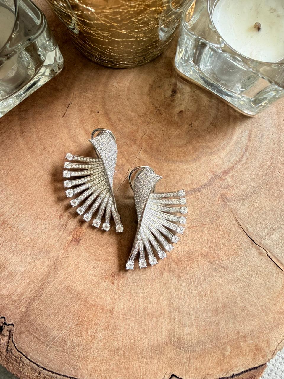 Silver fan-shaped earrings on a wooden surface with candles in the background