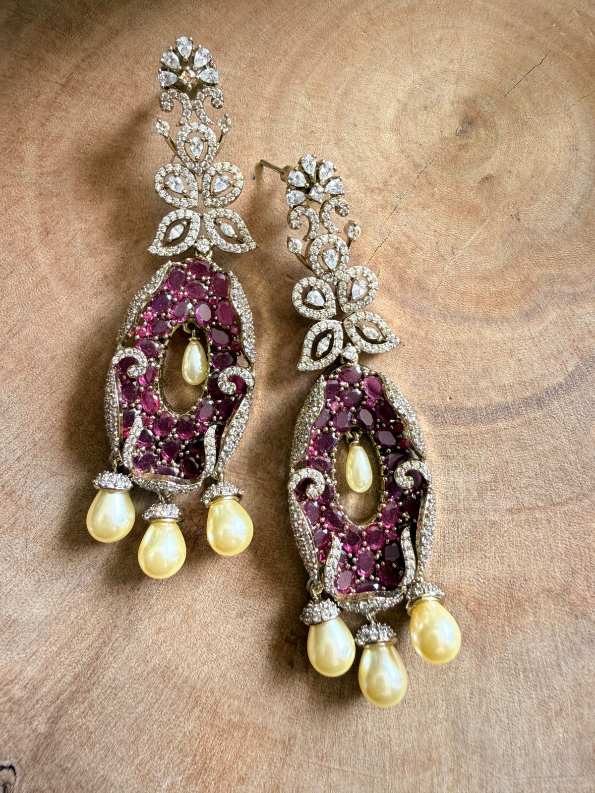 Ornate earrings with gemstones and pearls on a wooden surface