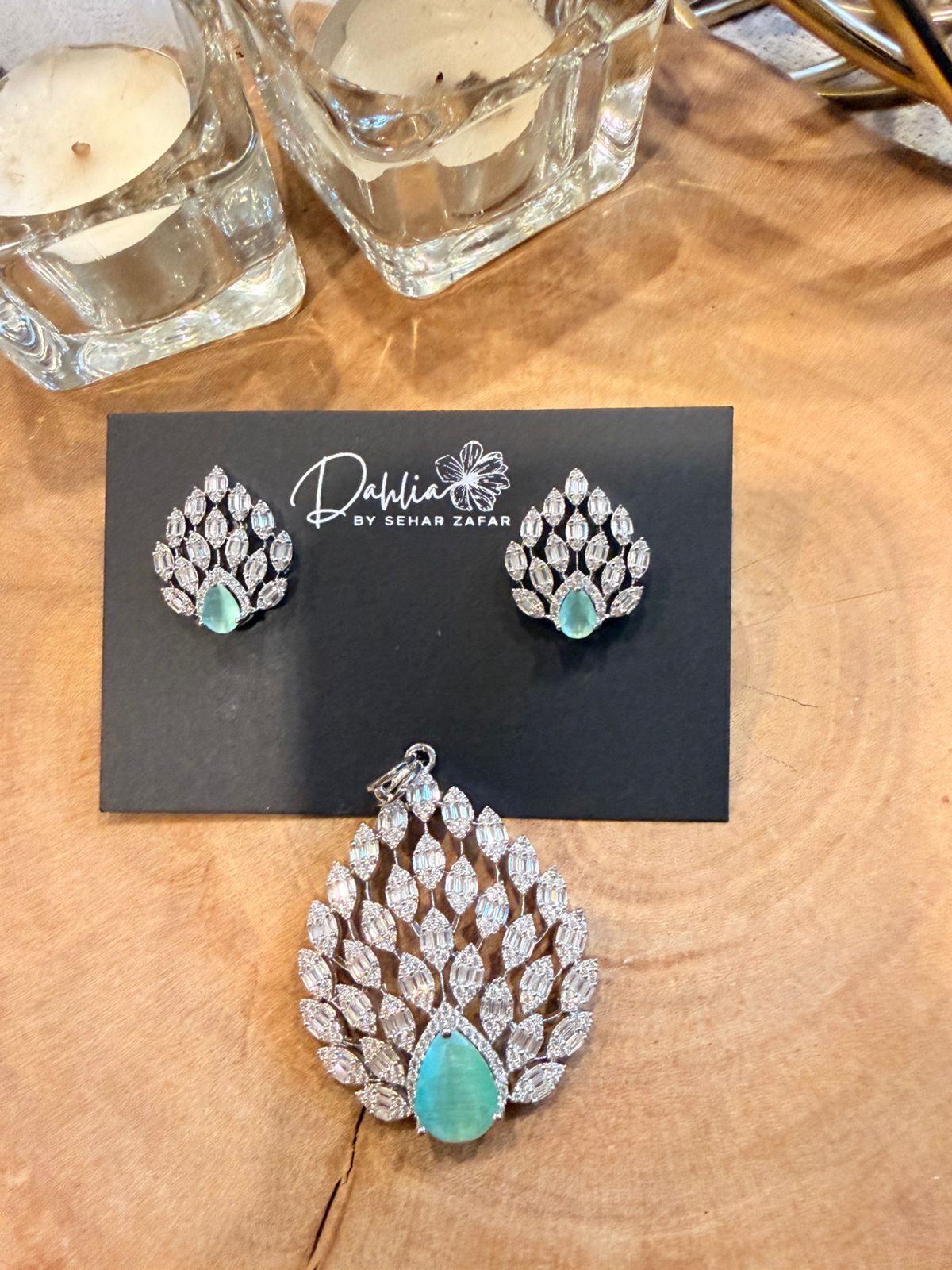 Jewelry set with earrings and a pendant on a wooden surface, featuring the brand 'Dahlia by Sneh Zafar'.