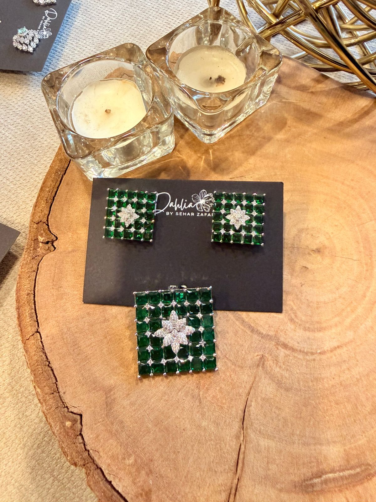 Green and silver earrings on a card with candles in the background
