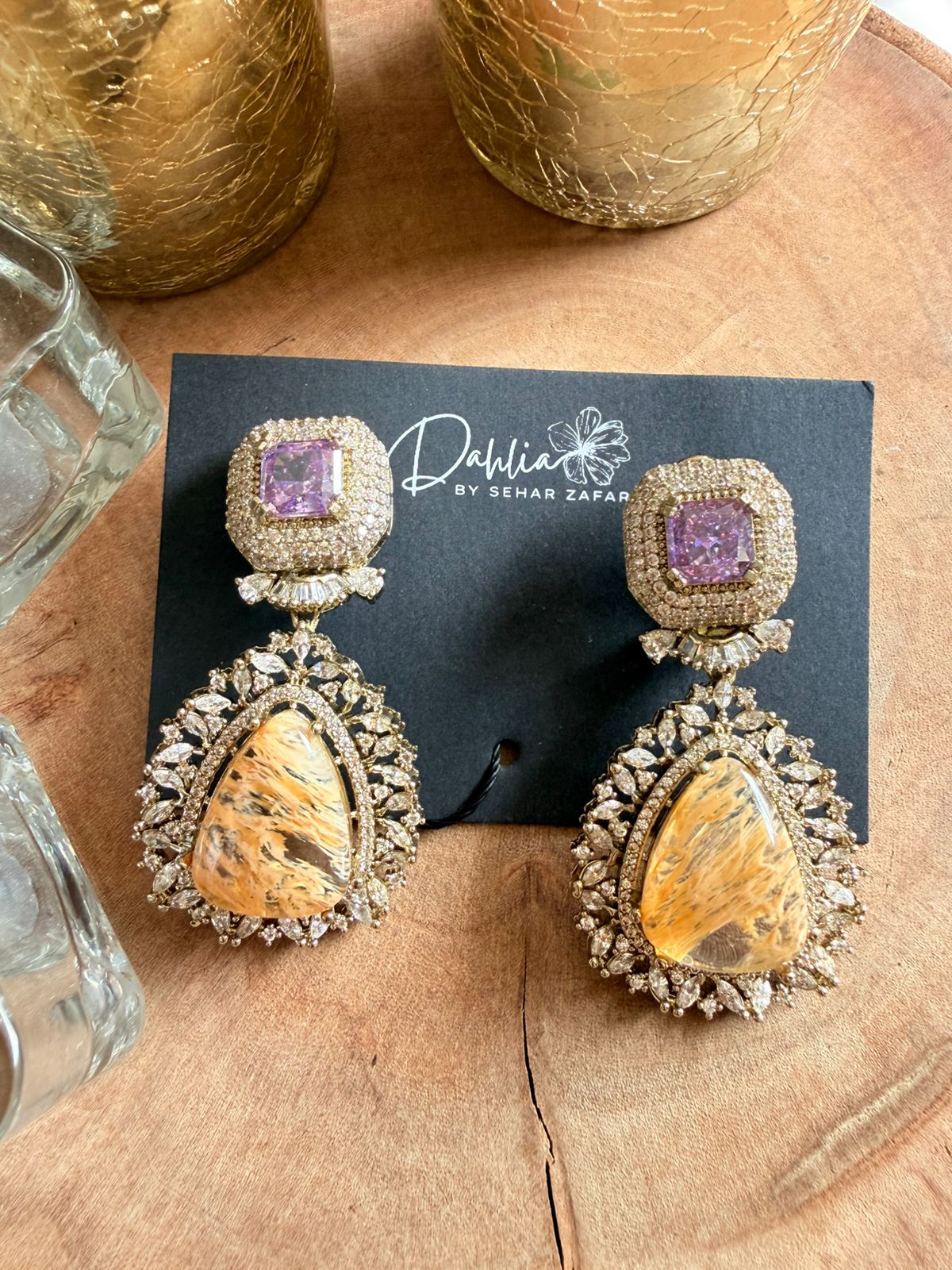 Pair of ornate earrings on a black card with 'Daphne' branding, placed on a wooden surface.