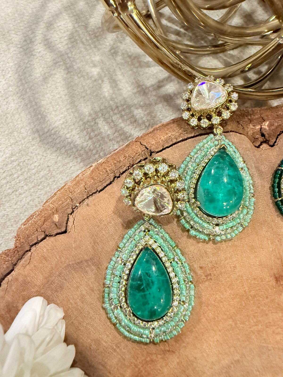Green teardrop earrings with gold accents on a textured surface