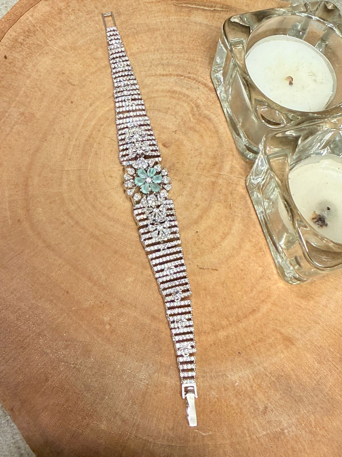 Decorative bracelet with gemstones on a wooden surface next to a candle holder.