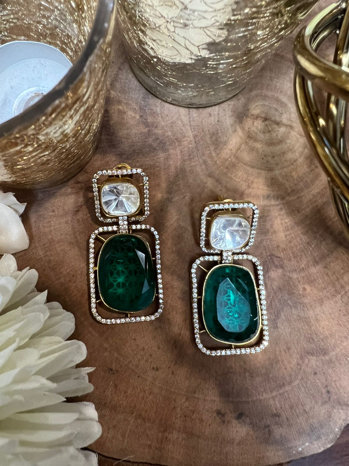 Pair of earrings with green gemstones and clear stones on a wooden surface.