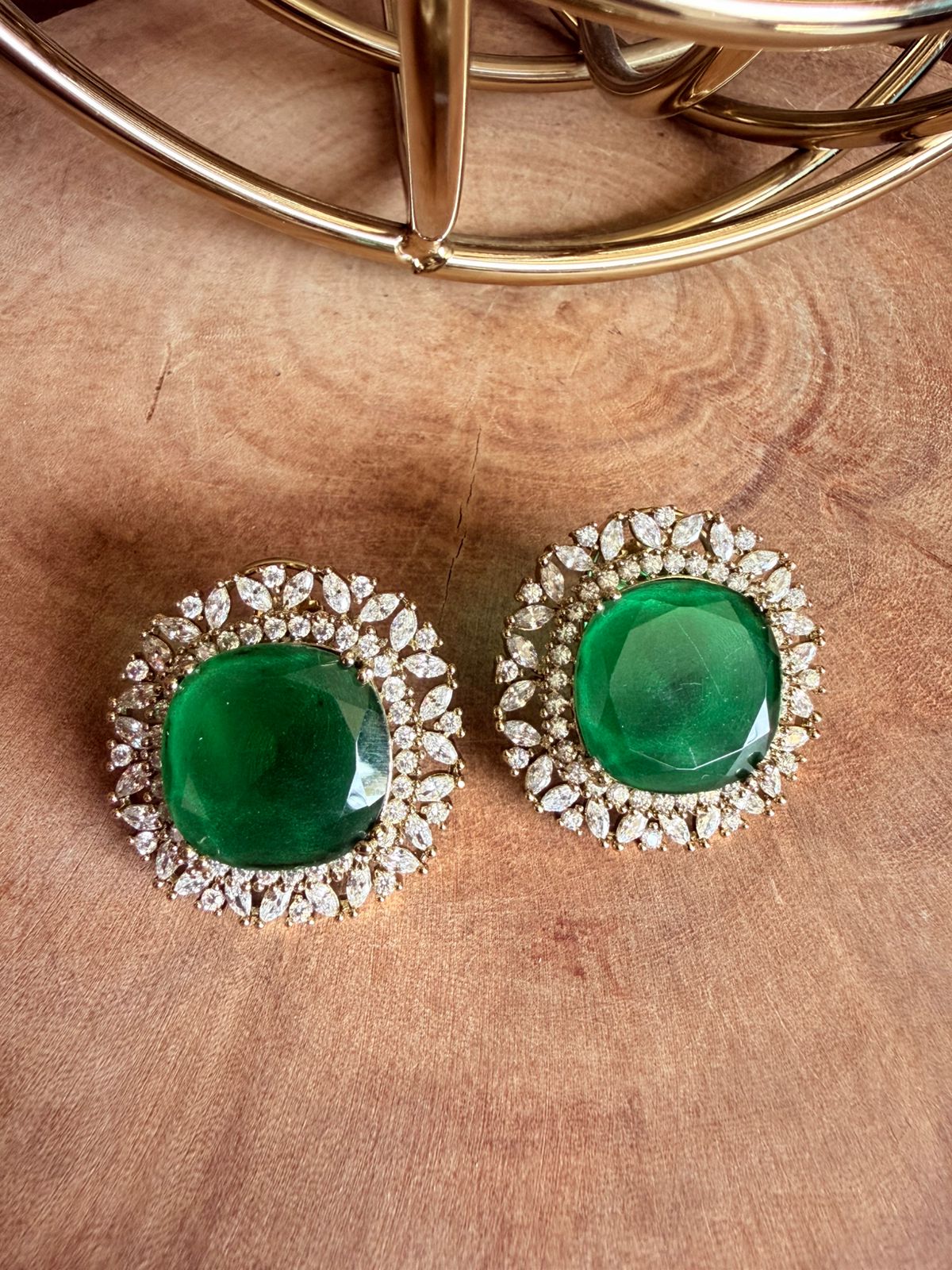 Pair of earrings with green gemstones and diamond-like accents on a wooden surface.
