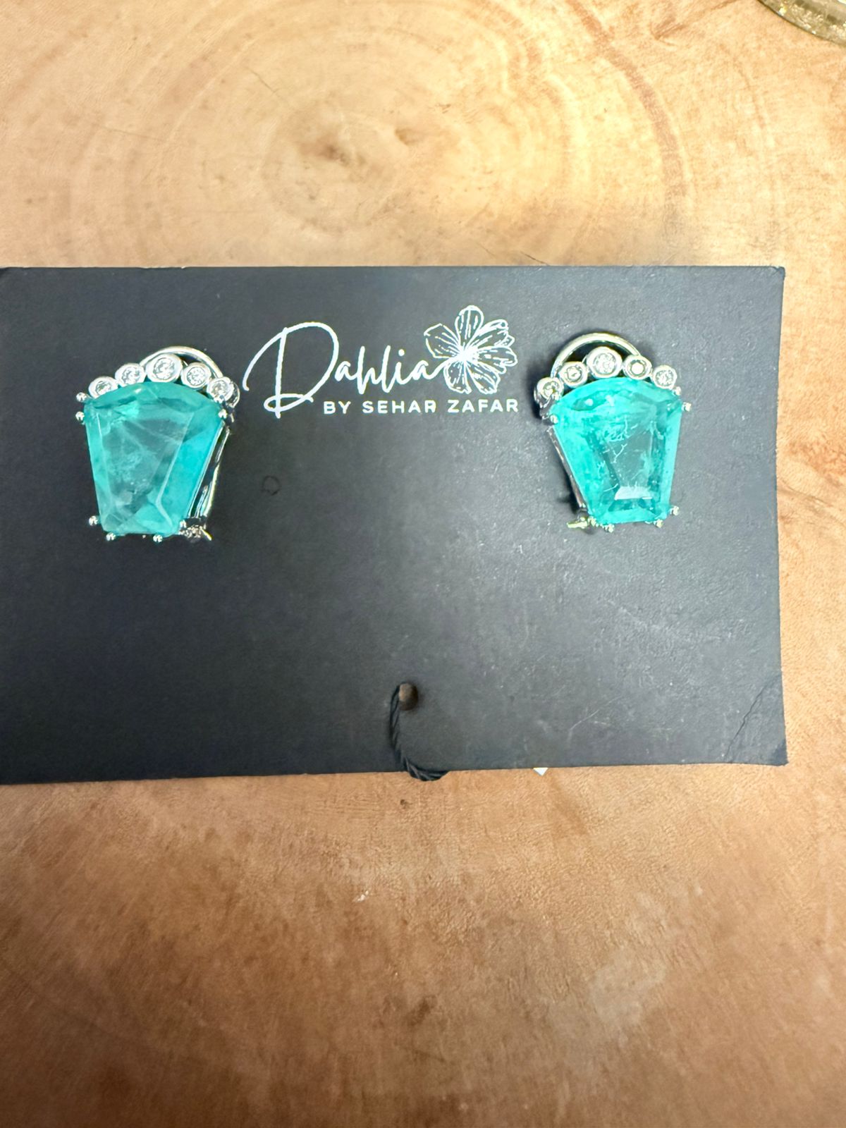 Turquoise earrings on a black card with 'Dahlia by Sehar Zafar' branding, placed on a wooden surface.