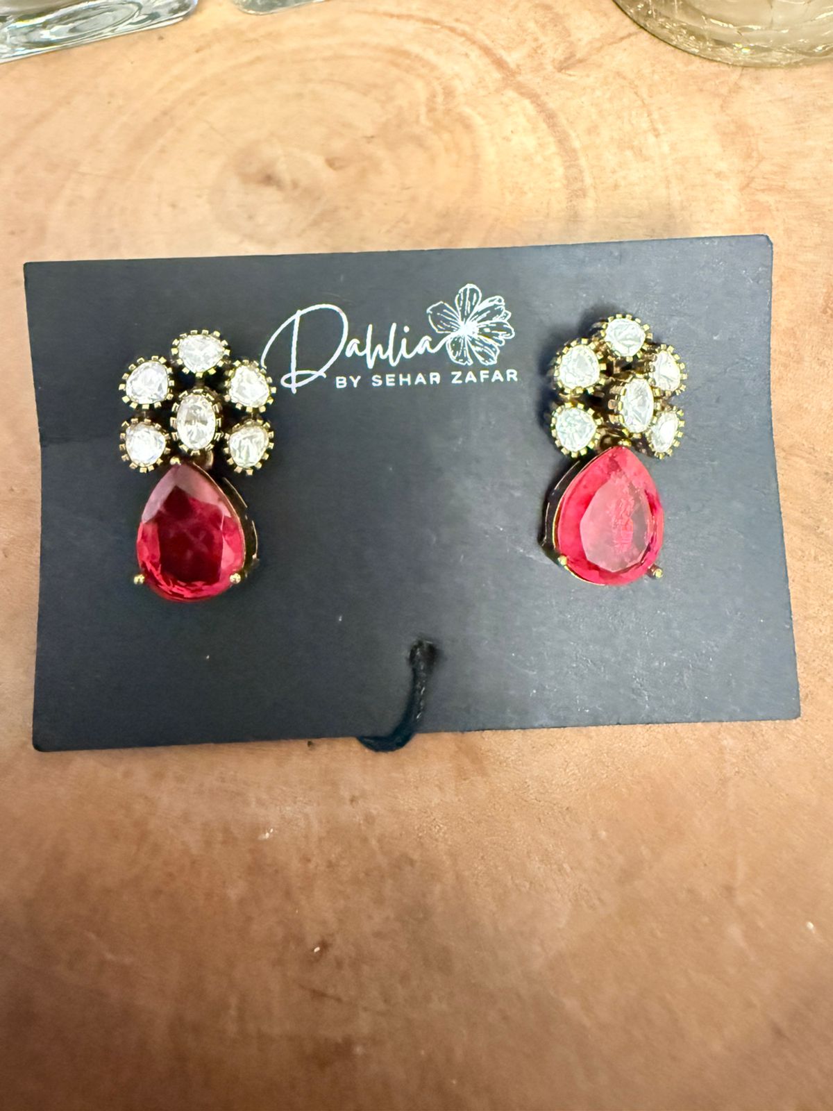 Red teardrop earrings with gold accents on a black card with 'Dahlia by Sehar Zafar' branding.
