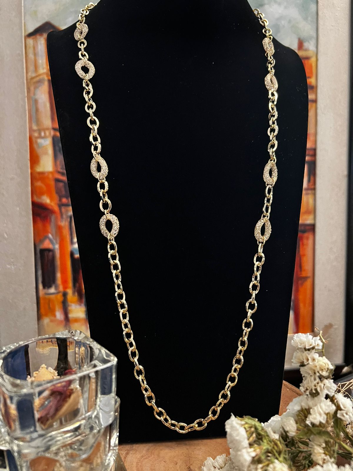 Long gold chain necklace with oval link detailing displayed on a black mannequin stand indoors