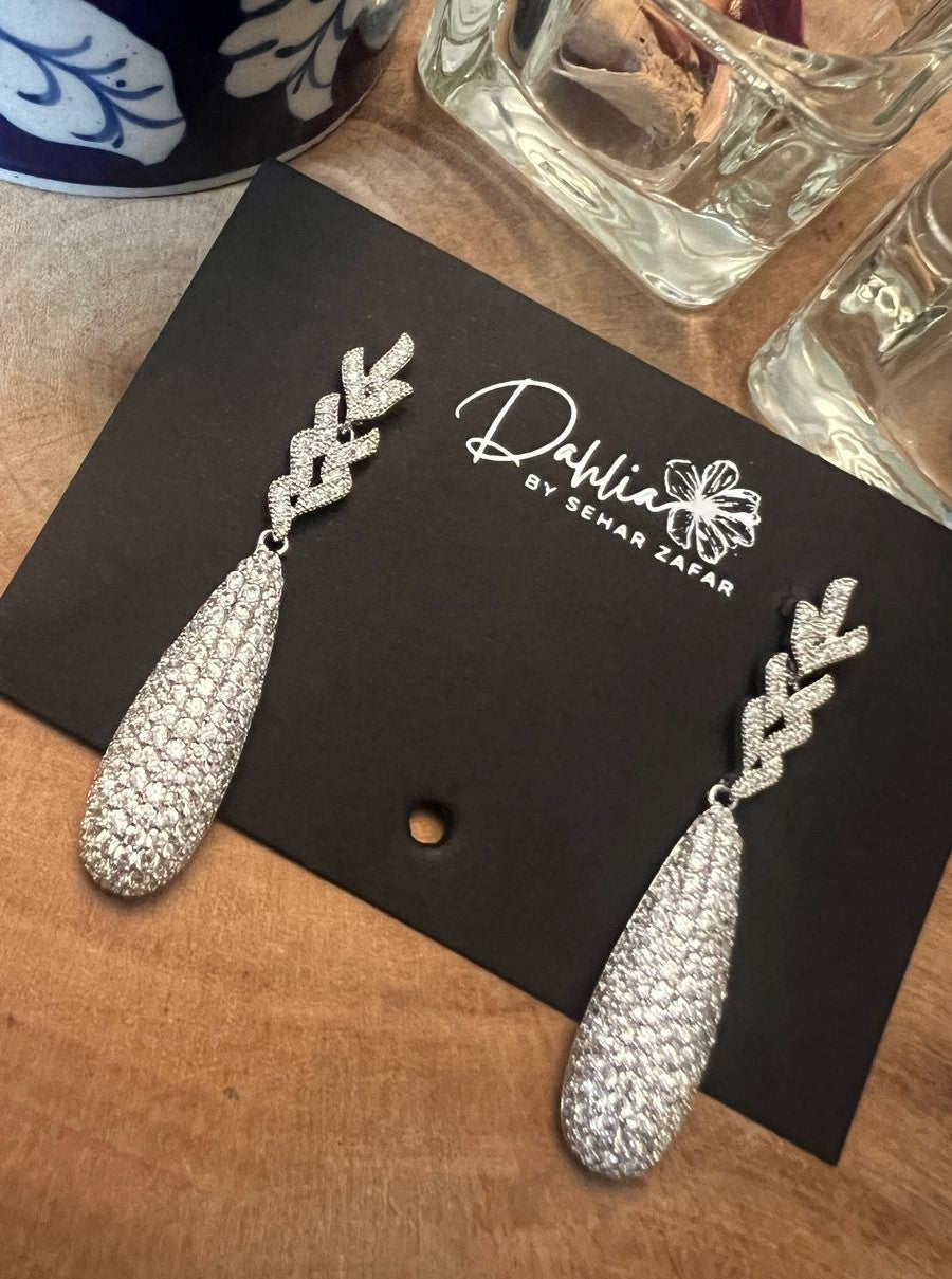 This image features a pair of sophisticated Syrah earrings, presented on a black card with the brand name "Dahlia". The earrings are designed with a striking copper base, embellished heavily with sparkling silver detailing that cascades elegantly downwards, creating a dazzling visual effect.