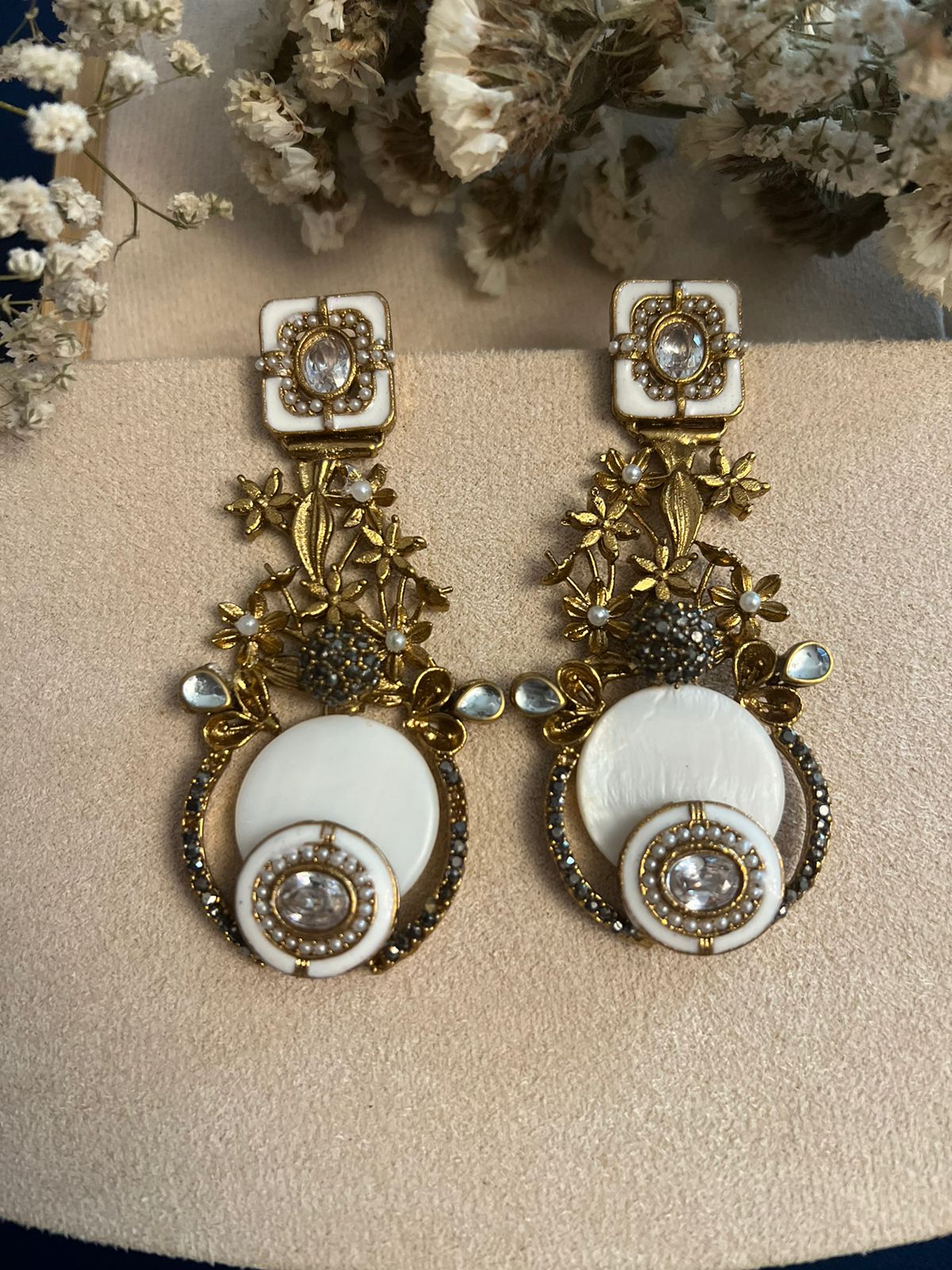 Gold detailed statement earrings with semi-precious stones and white accents on a soft background.
