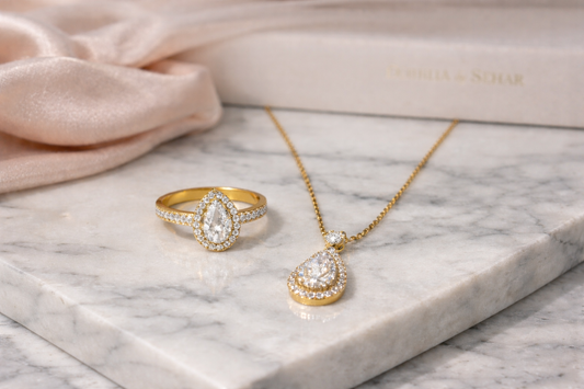 Elegant luxury gold jewellery set with pear shaped diamond ring and pendant necklace on marble background