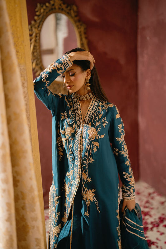 Woman wearing a teal embroidered traditional outfit styled with statement necklace and earrings in an elegant indoor setting