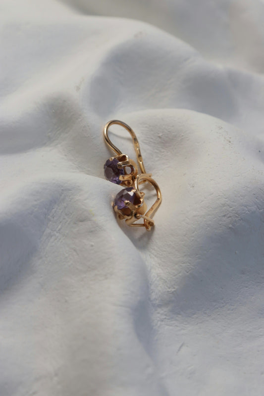 Golden earrings with purple gemstones on white surface.
