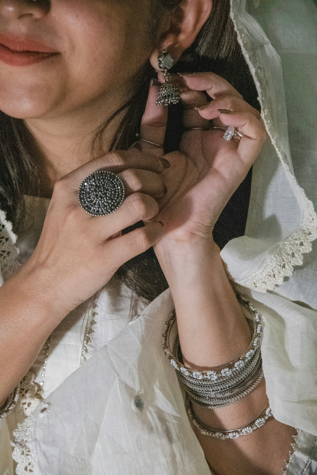 Woman adjusts ornate earring while wearing bangles and ring