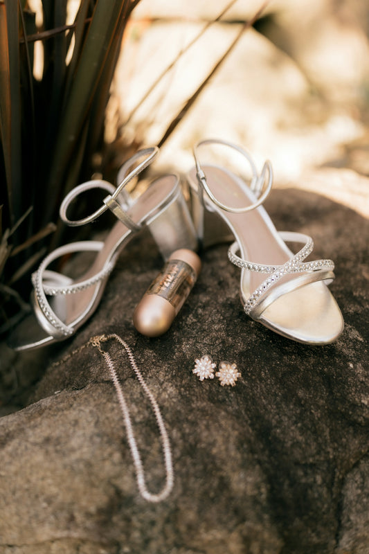 Silver heels, necklace, earrings, and perfume on rock