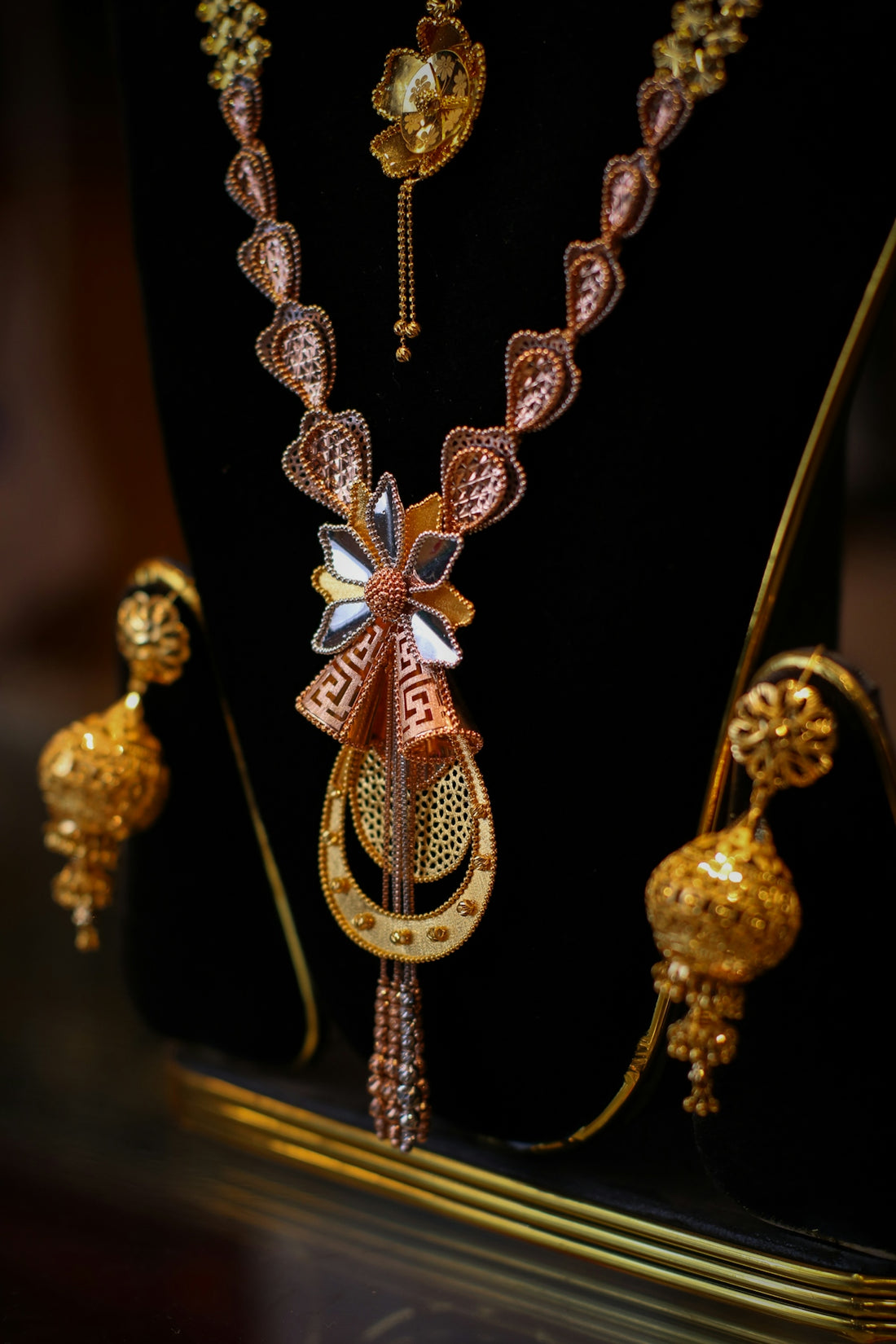 A gold necklace with a floral pendant and matching jhumka earrings on display