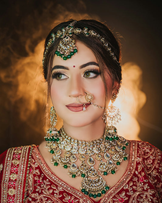A woman wearing traditional red bridal attire and ornate gold and green jewelry
