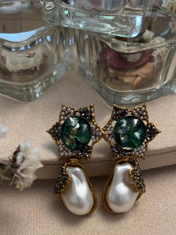 This image displays a pair of elegant earrings named "Rania," featuring a sophisticated design with gold detailing and emerald semi-precious stones set in a copper-based metal. The earrings are designed with a captivating star-shaped top, embellished with small pearls and larger emerald stones, leading down to prominent pearl drops.