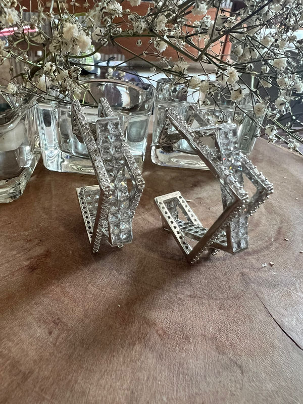 This image features a pair of elegant candle holders named "Noor," inspired by the brilliant cut of a diamond. These copper-based holders exhibit a striking transparency, much like polished gemstones, with intricate detailing that enhances their sophisticated allure.