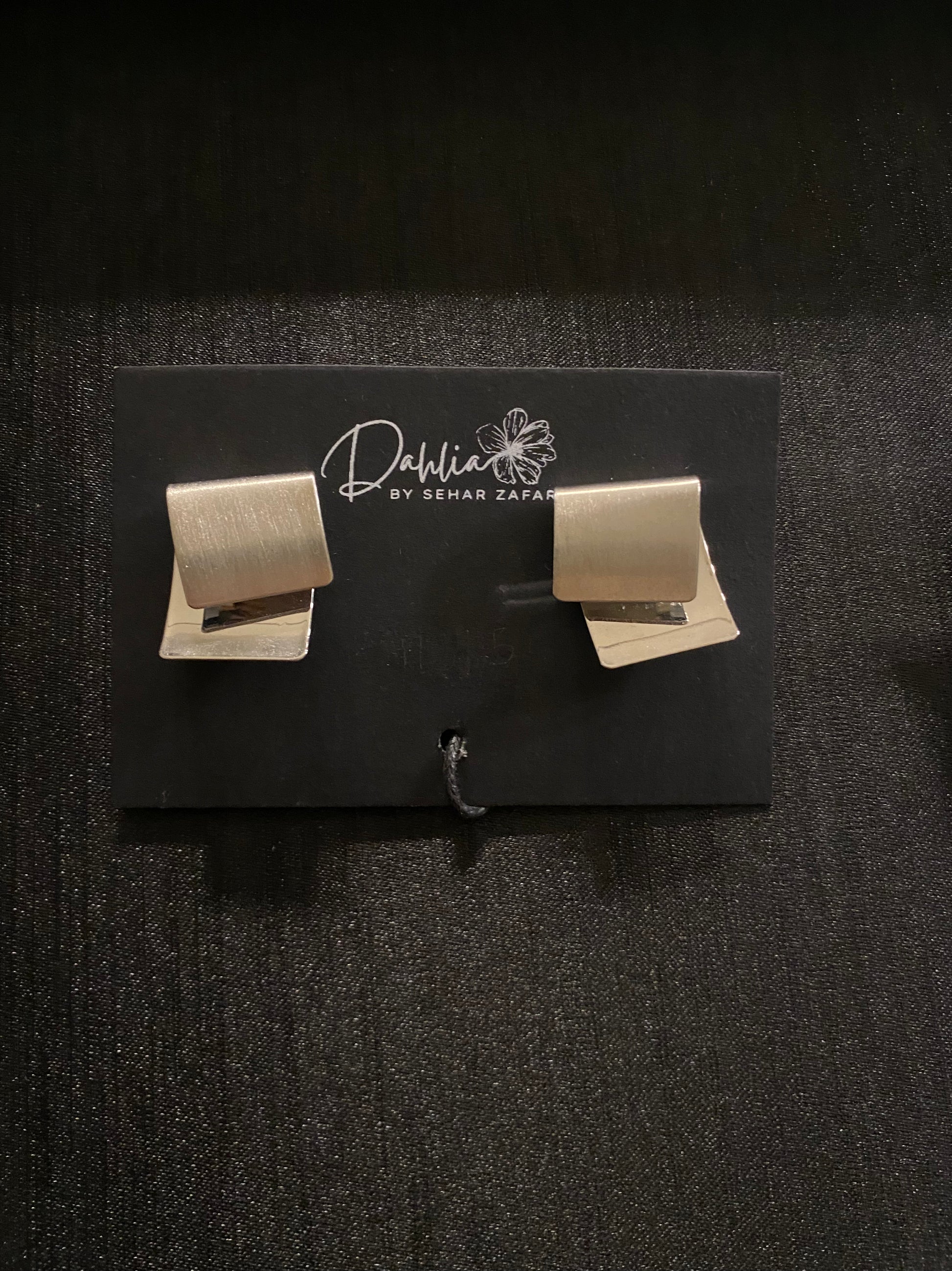 Matte gold geometric stud earrings displayed on a black Dahlia by Sehar Zafar card.
