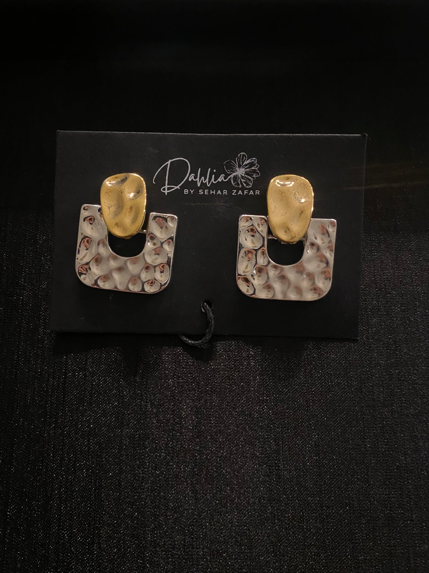 Hammered gold U-shaped earrings with sculpted tops on black branded card