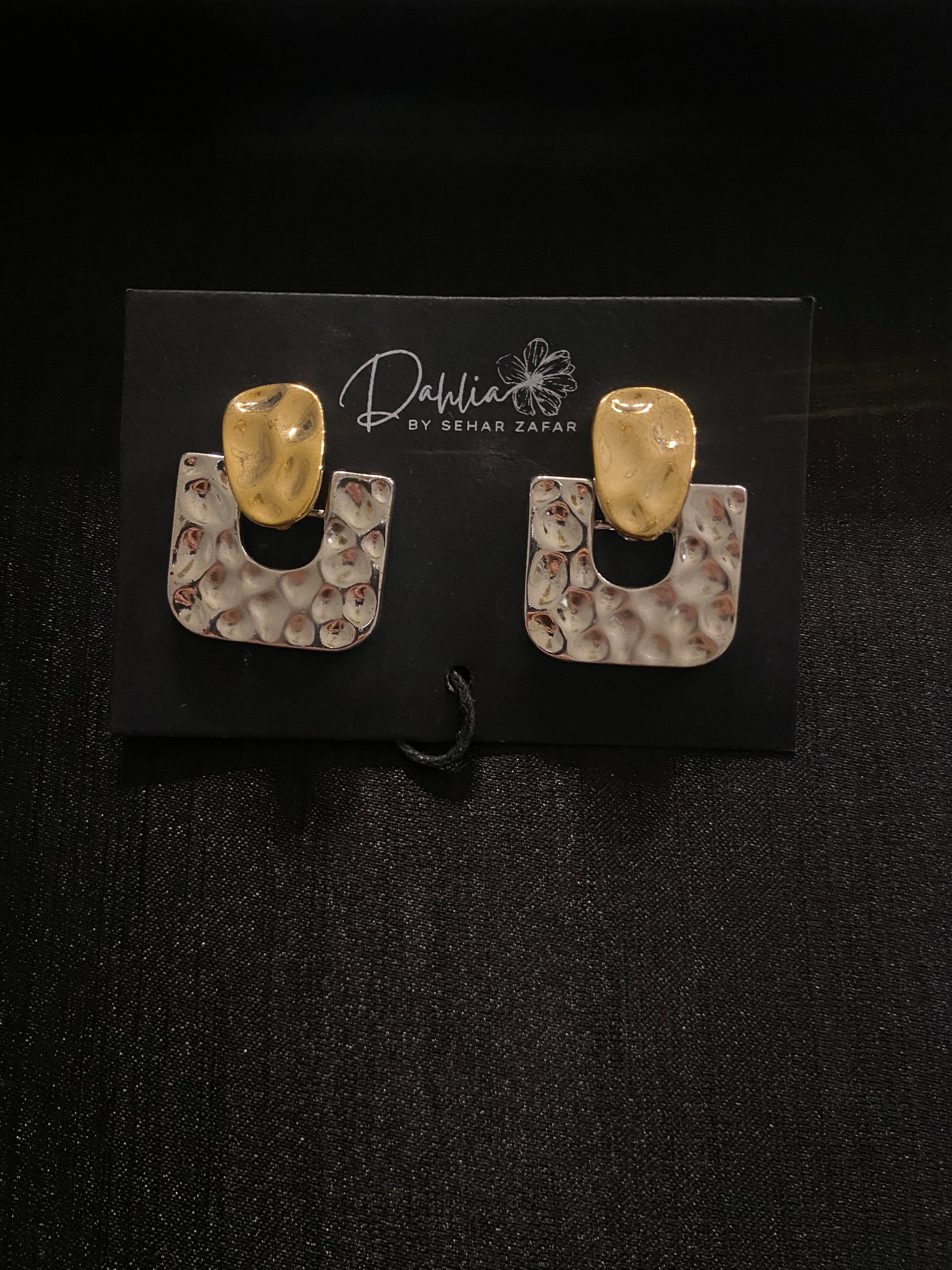 Hammered gold U-shaped earrings with sculpted tops on black branded card