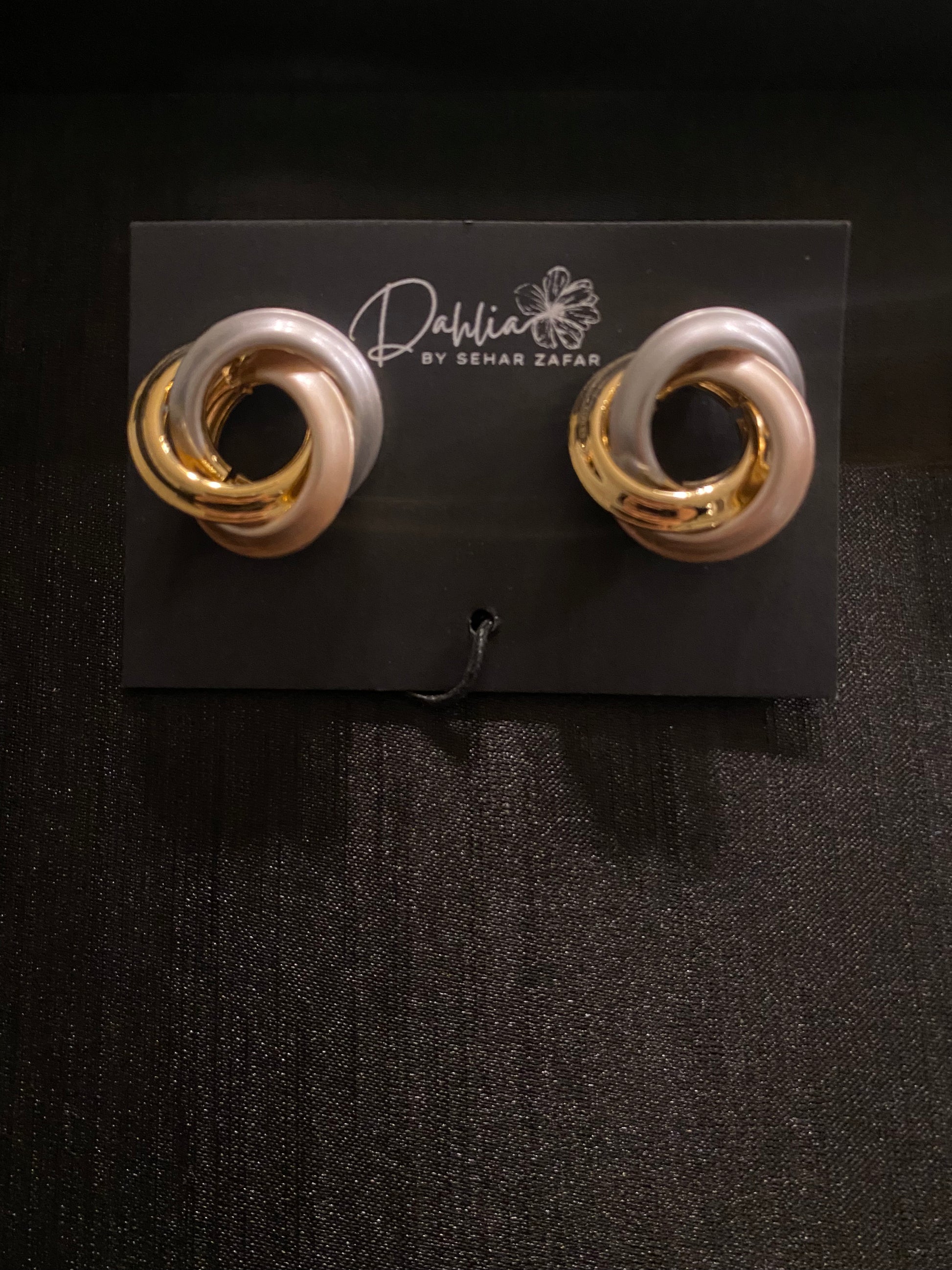 Twisted gold and pearlescent pink loop earrings on black branded card